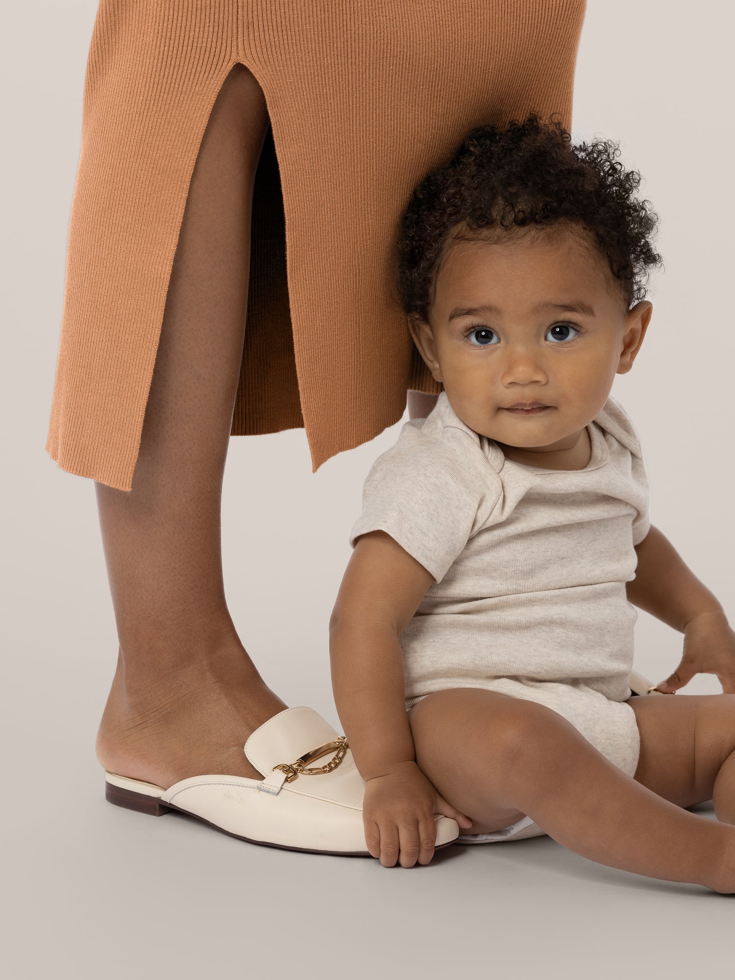 Close-up view of bottom on the 2-in-1 Maternity & Nursing Midi Dress in Camel, showing side slit, with baby sitting between model's feet