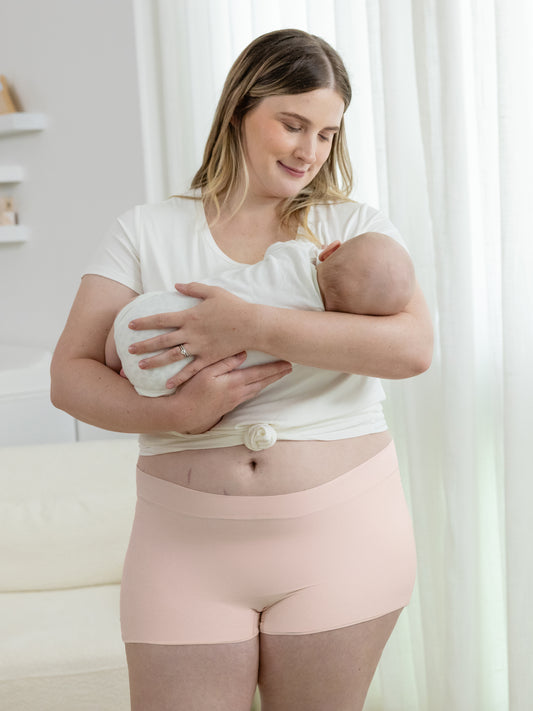 Model holding her baby while wearing the Everyday Nursing T-shirt in White and the Grow with Me™ Maternity & Postpartum Boyshort in Soft Pink. @model_info: Piper is wearing an X-Large.