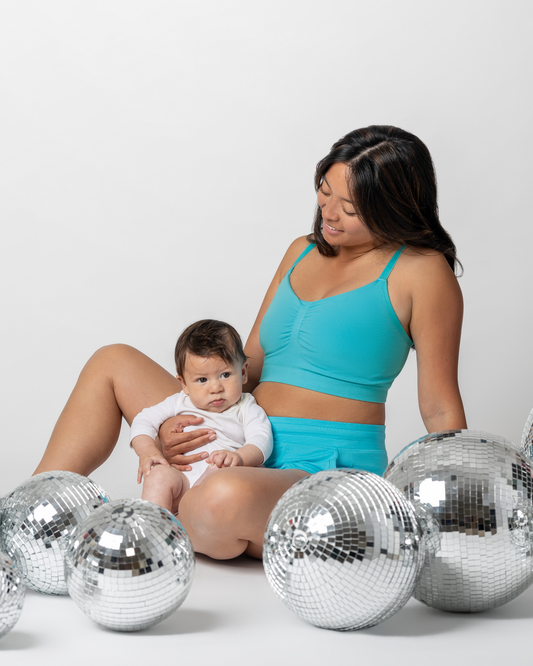 Model sitting with baby next to disco balls wearing the Sublime® Bamboo Hands-Free Pumping Lounge & Sleep Bra in Aquamarine with matching Bamboo Maternity & Postpartum Lounge Short @model_info:Hillary is wearing a Small.