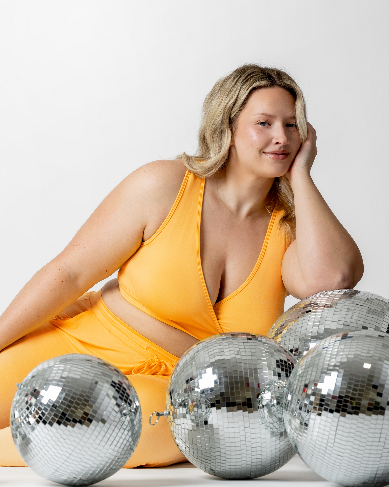 Model resting on disco ball while wearing French Terry Racerback Nursing & Sleep Bra in Marigold with matching Everyday Lounge Joggers @model_info:Austen is wearing an X-Large Busty.