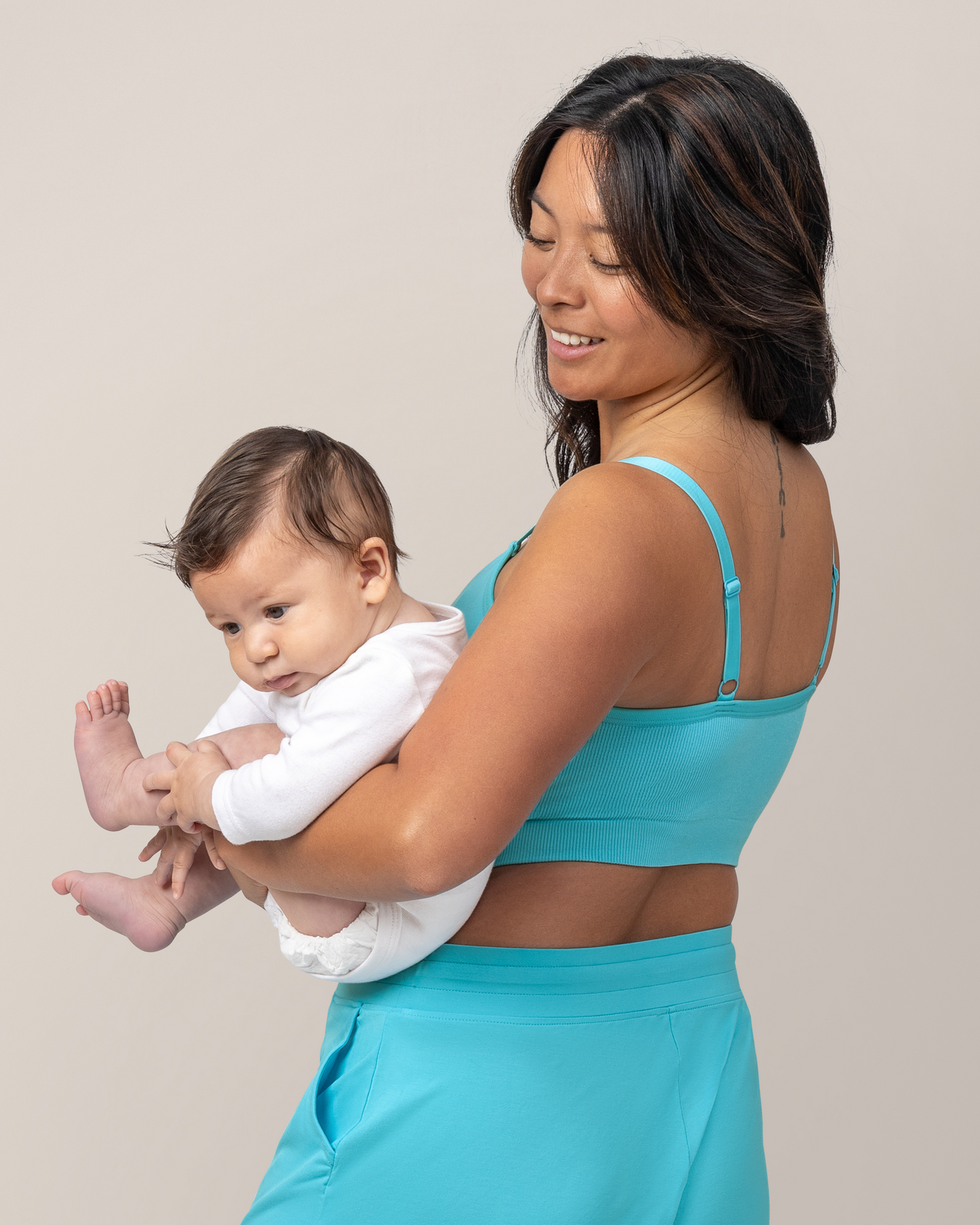 Side back view of model wearing the Sublime® Bamboo Hands-Free Pumping Lounge & Sleep Bra in Aquamarine and holding baby