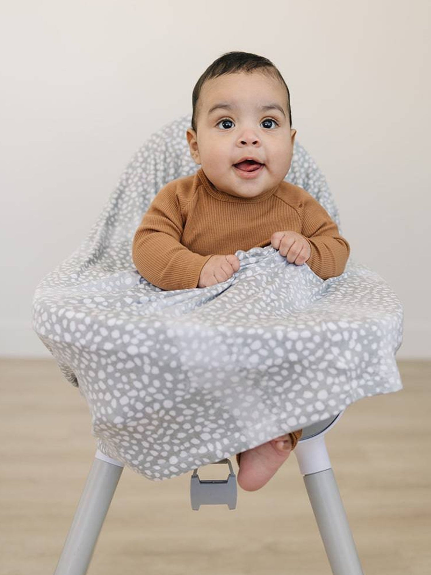 The Bebe au Lait - 5-in-1 Multi-Use Nursing Cover in Animal Ombre covering surfaces of a high chair with baby sitting