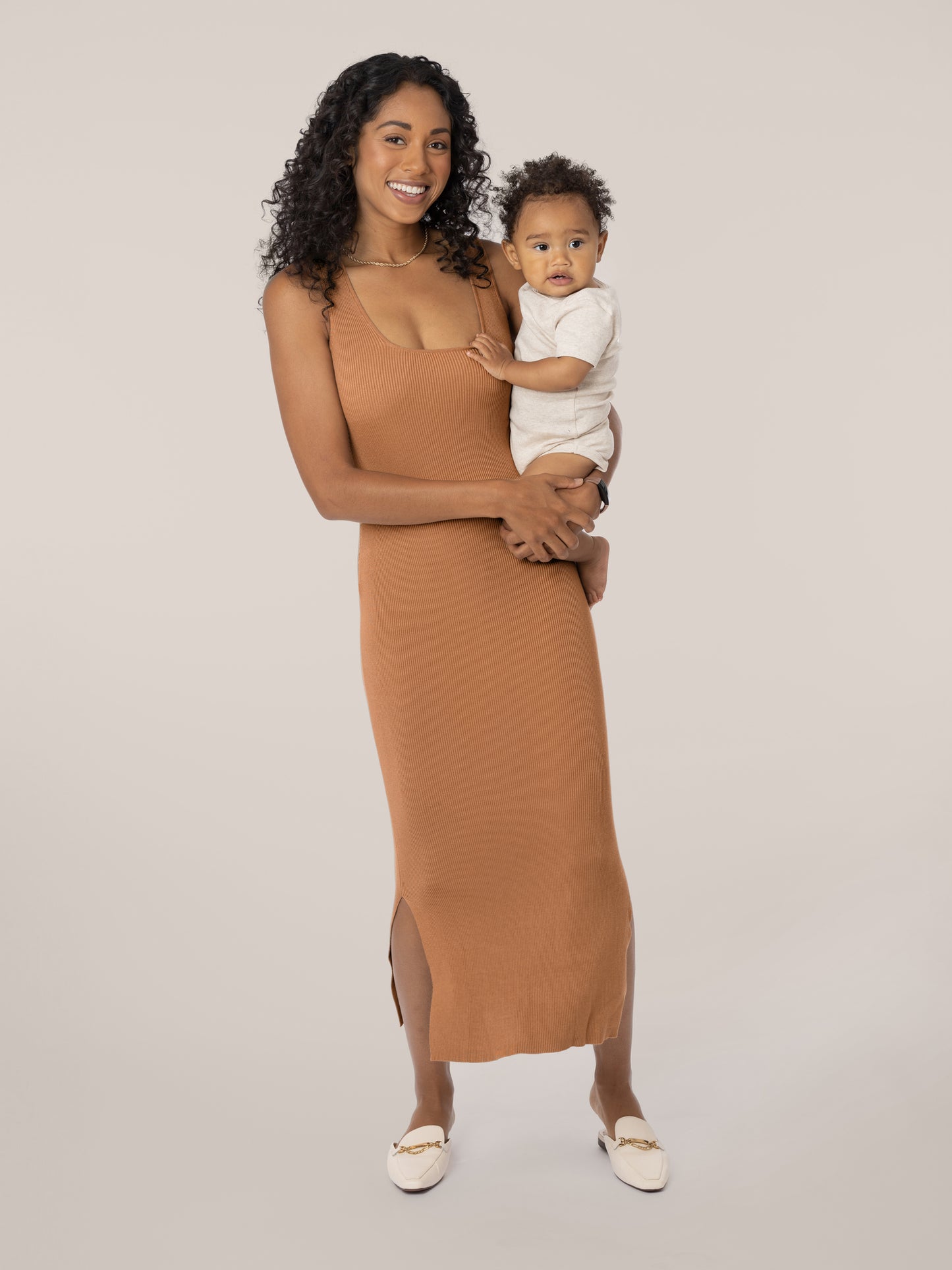 Front view of model wearing the 2-in-1 Maternity & Nursing Midi Dress in Camel without top long-sleeve cropped layer, holding baby