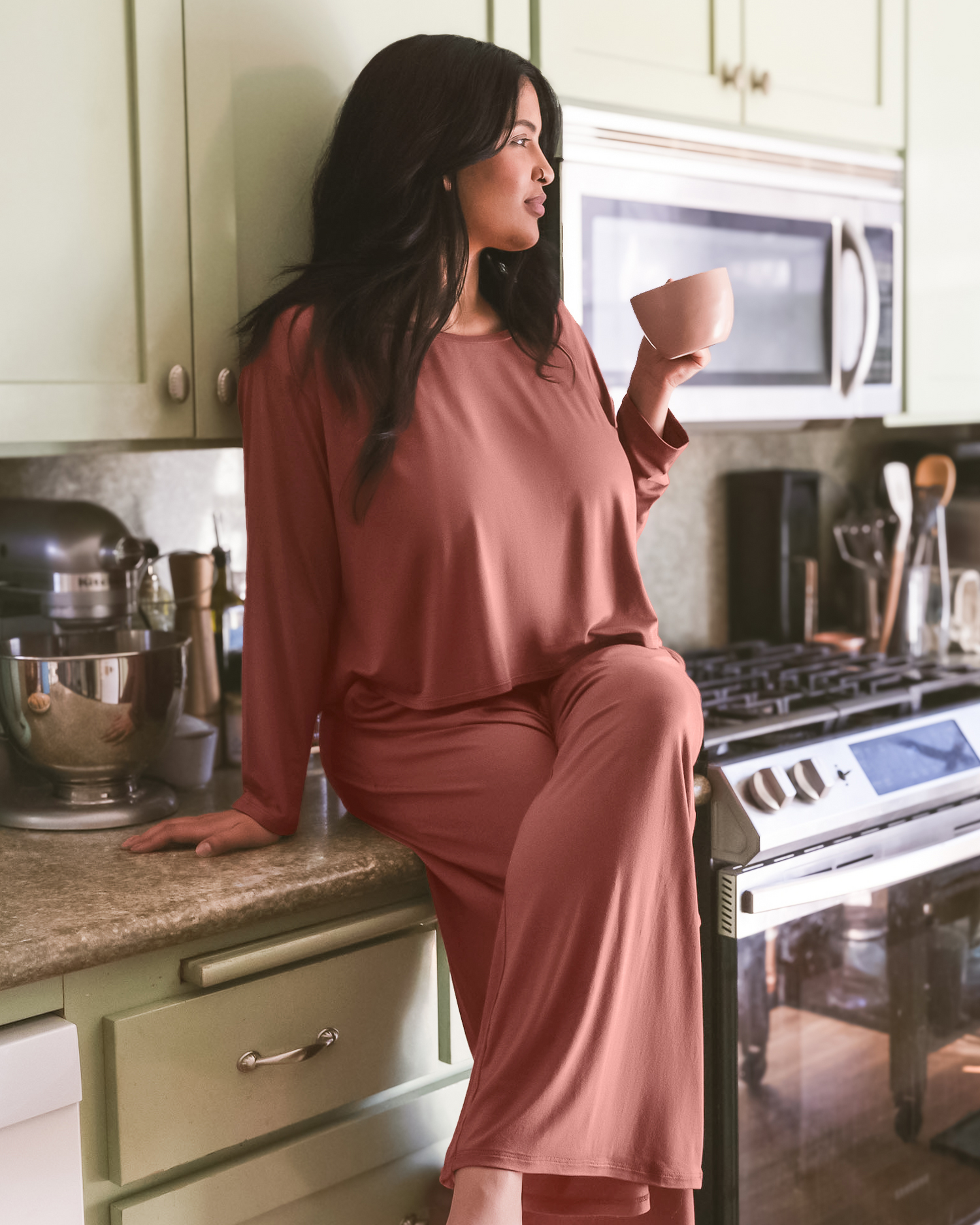 Model sitting in kitchen wearing the Aria Bamboo Casual Cropped long Sleeve Top in Redwood with the matching Aria Bamboo Casual Lounge Short @model_info:Betsabe is wearing a Medium.