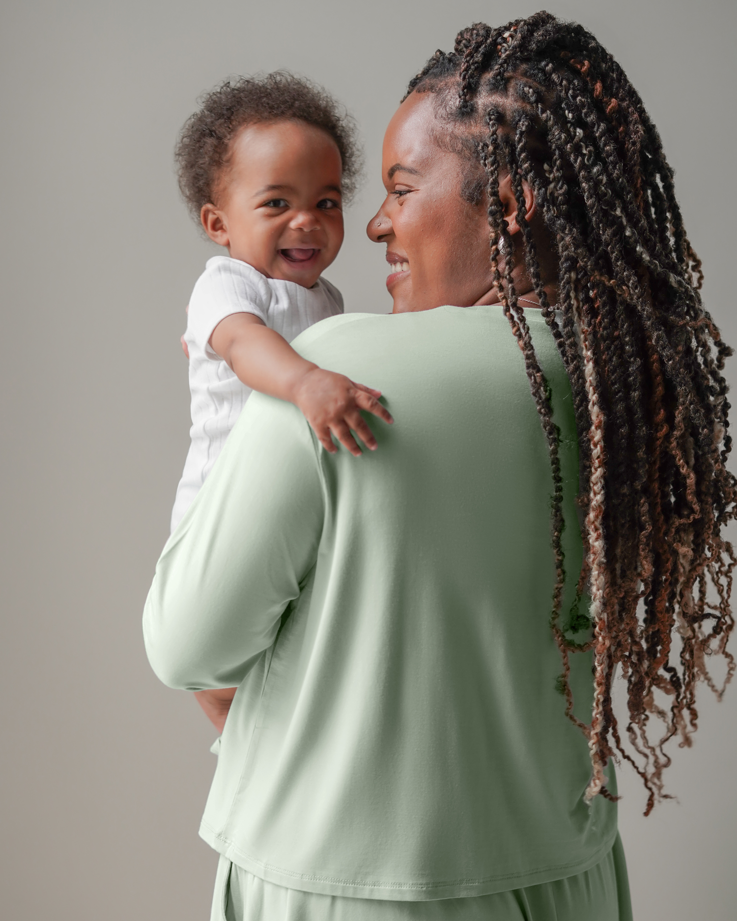 3/4 back view of model wearing the Aria Bamboo Casual Cropped Long Sleeve Top in Aqua Mist, holding baby looking over her shoulder