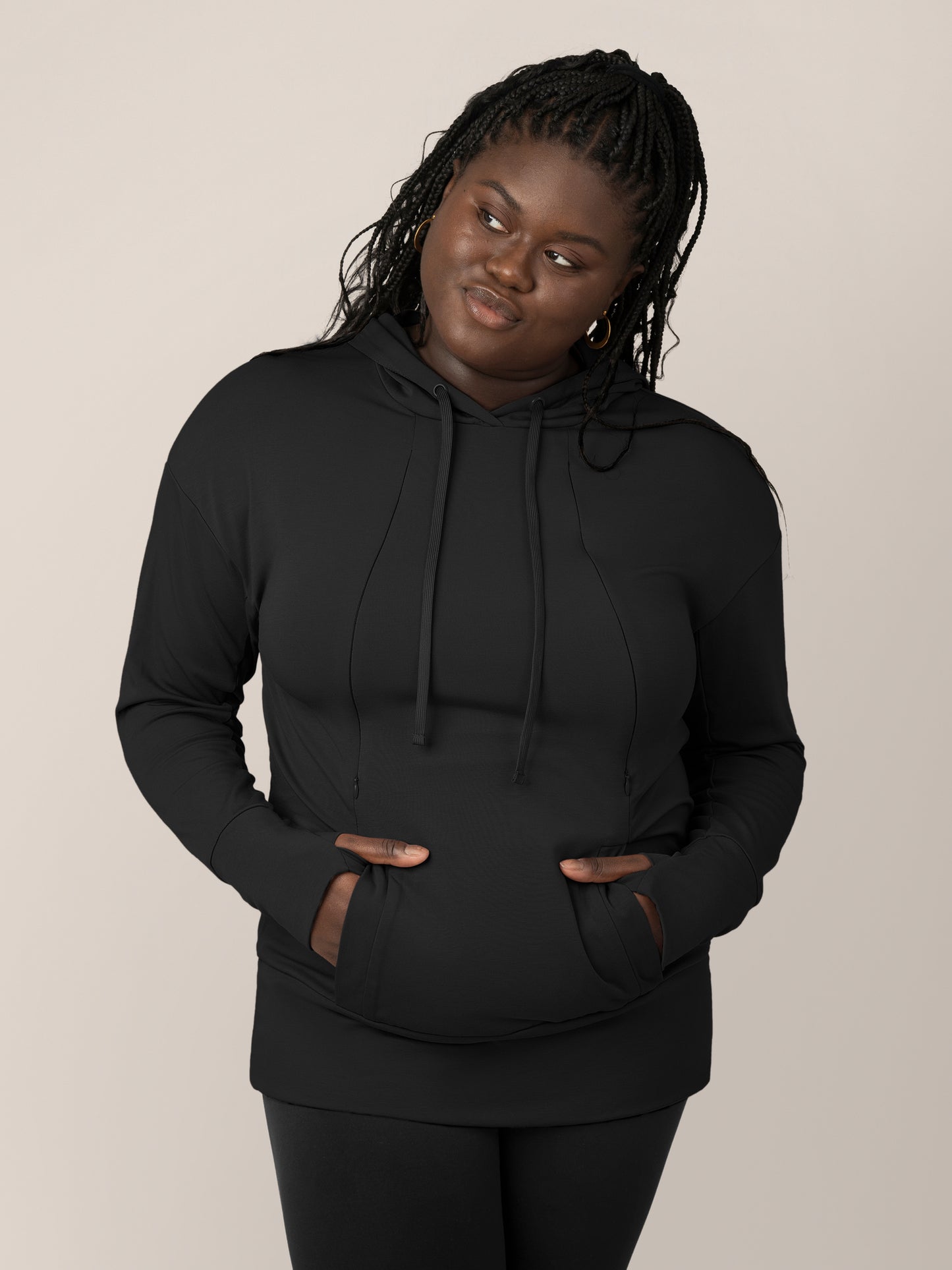 Front view of model wearing the Bamboo Maternity & Nursing Hoodie in black, with hands in pocket and thumbs through thumb holes@model_info:Bintou is wearing an X-Large.