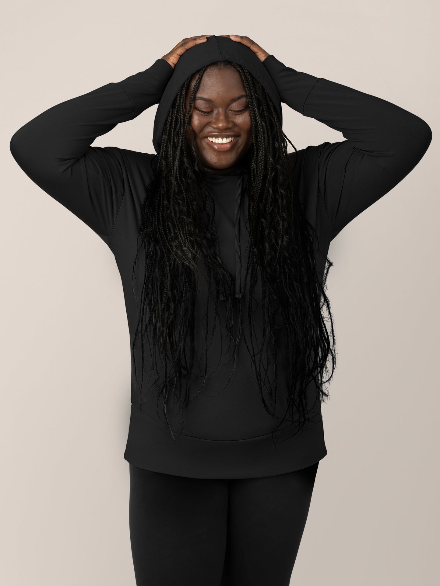 Front view of model wearing the Bamboo Maternity & Nursing Hoodie in black, with hood on and hands on head