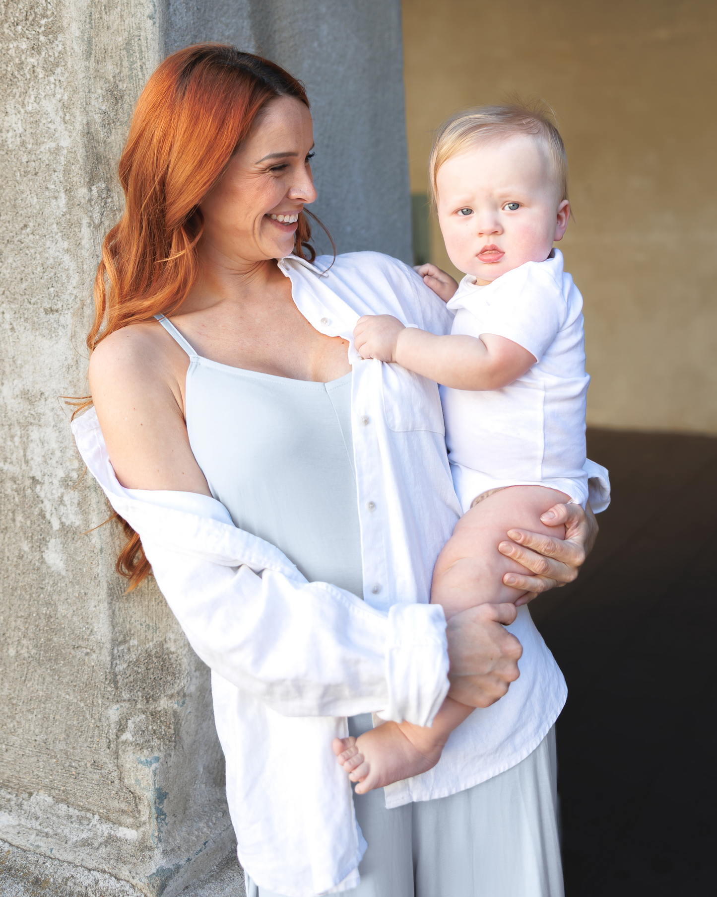 Model outside holding baby and wearing the Charlie Maternity & Nursing Romper in French Blue, paired with open oversized button down shirt