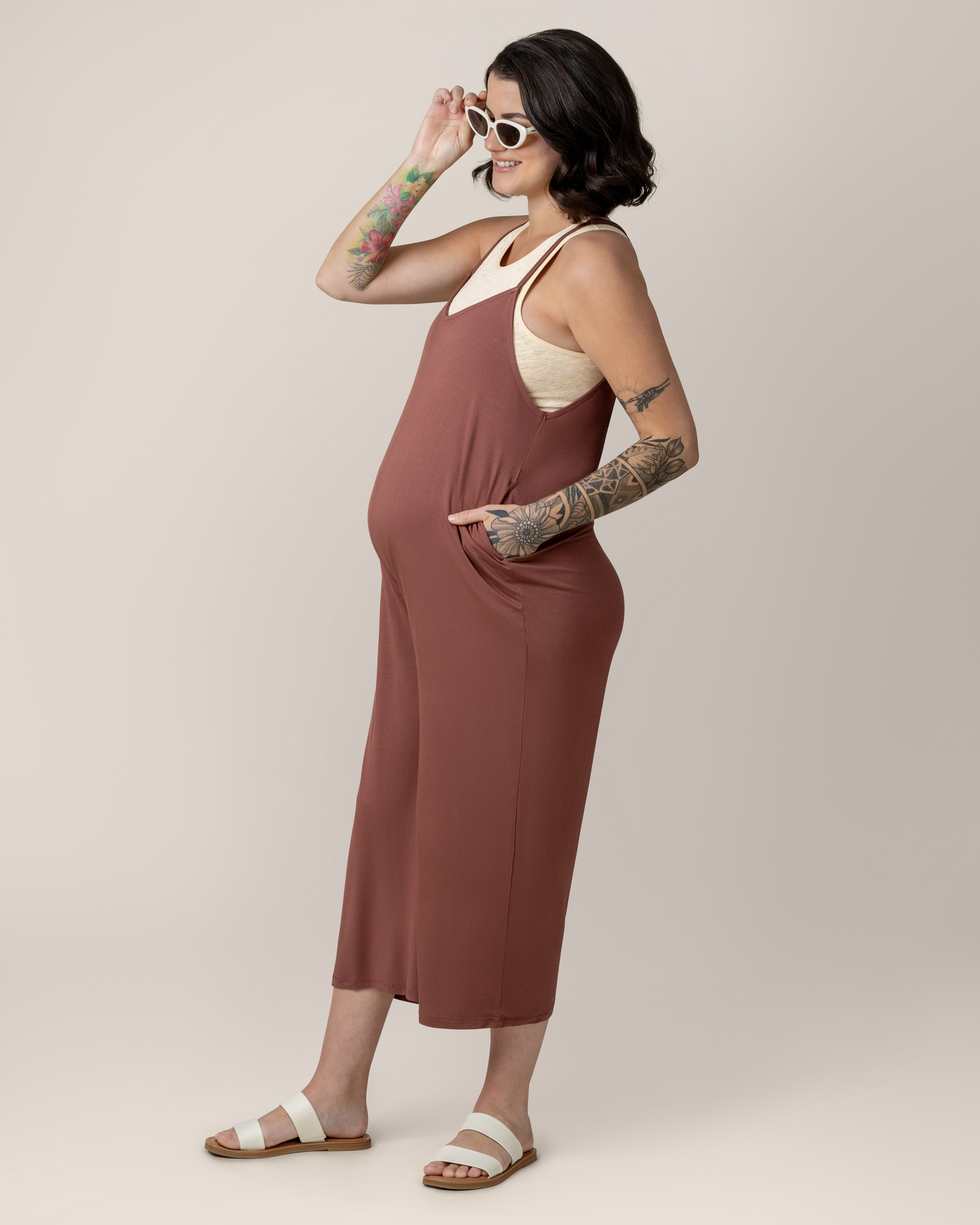 Side view of pregnant model with hand in pocket wearing the Charlie Maternity & Nursing Romper in Redwood, paired with Sublime® Bamboo Maternity & Nursing Longline Bra Top in Oatmeal Heather and flat sandals. @model_info:Emily is 5'8" and wearing a Medium.