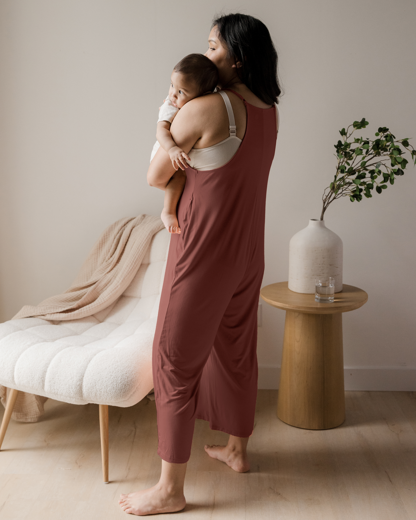 3/4 back view of model holding baby while wearing the Charlie Maternity & Nursing Romper in Redwood