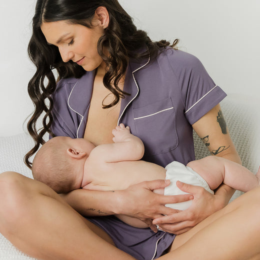 Model wearing the Clea Bamboo Short Sleeve Pajama Set in Granite, sitting cross-legged and nursing baby.