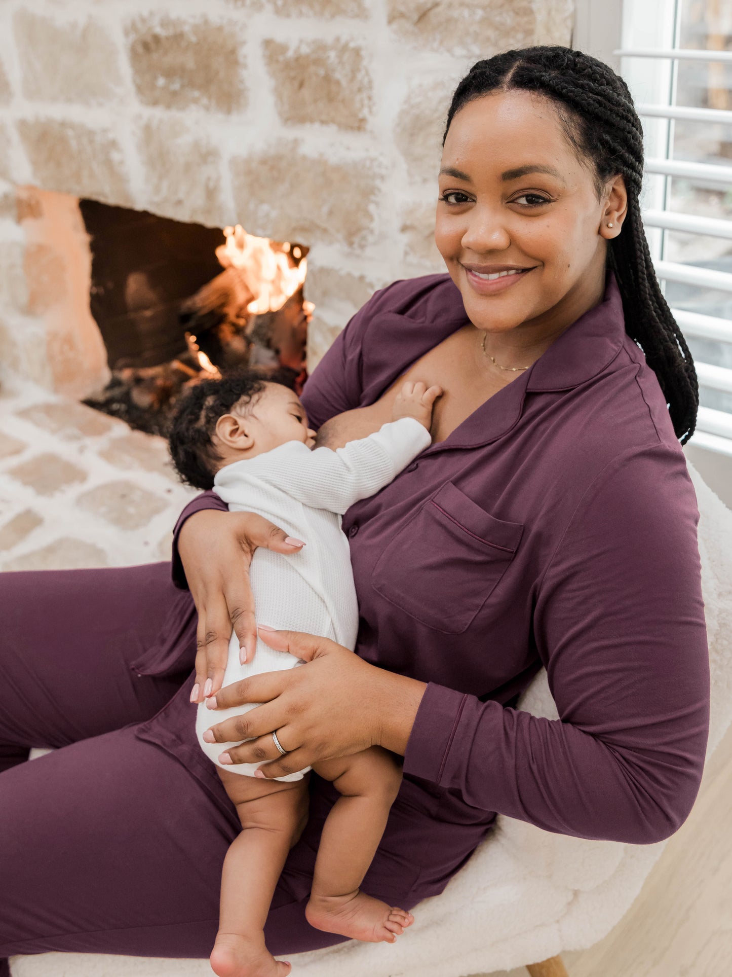 Close up of model sitting in chair wearing the Clea Bamboo Long Sleeve Pajama Set in Burgundy Plum and nursing baby.