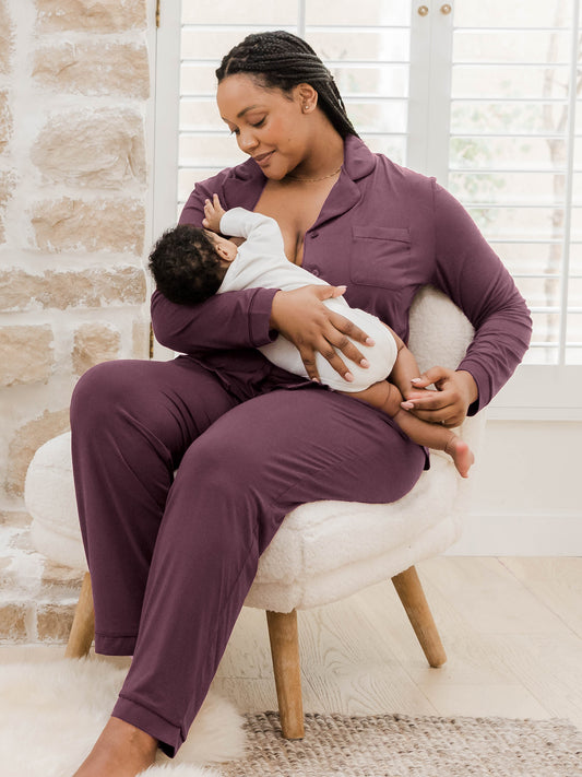 Model sitting in chair wearing the Clea Bamboo Long Sleeve Pajama Set in Burgundy Plum and nursing baby. @model_info:Roxanne is 5'9" and wearing a Large.