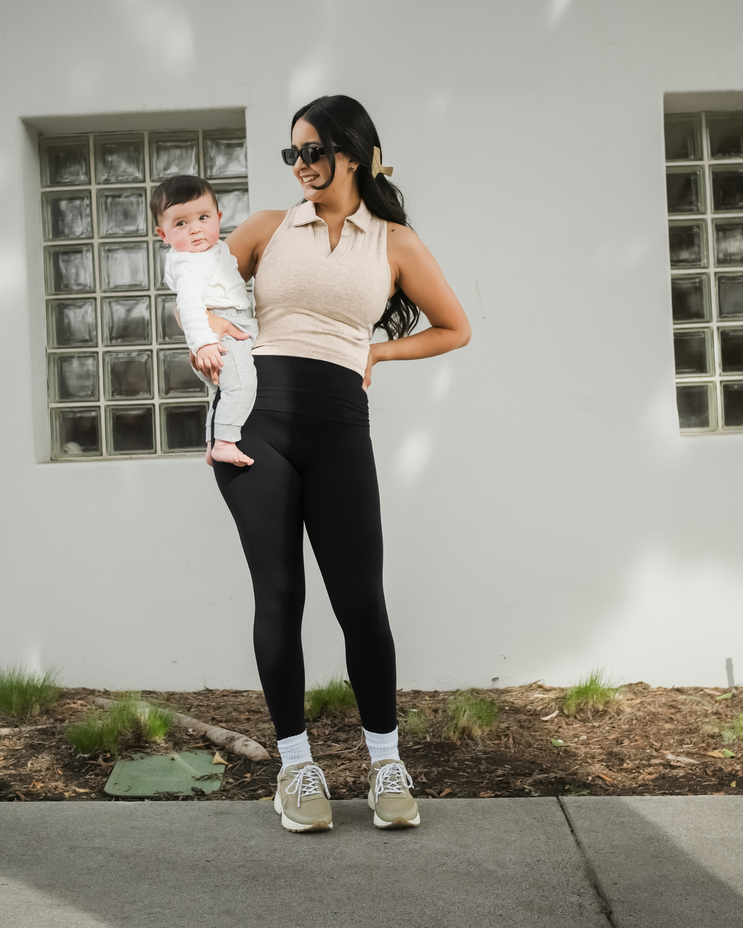 Full body front view of model wearing the Sublime® Bamboo Collared Maternity & Nursing Longline Bra Top in Oatmeal Heather, paired with leggings and tennis shoes, and holding baby