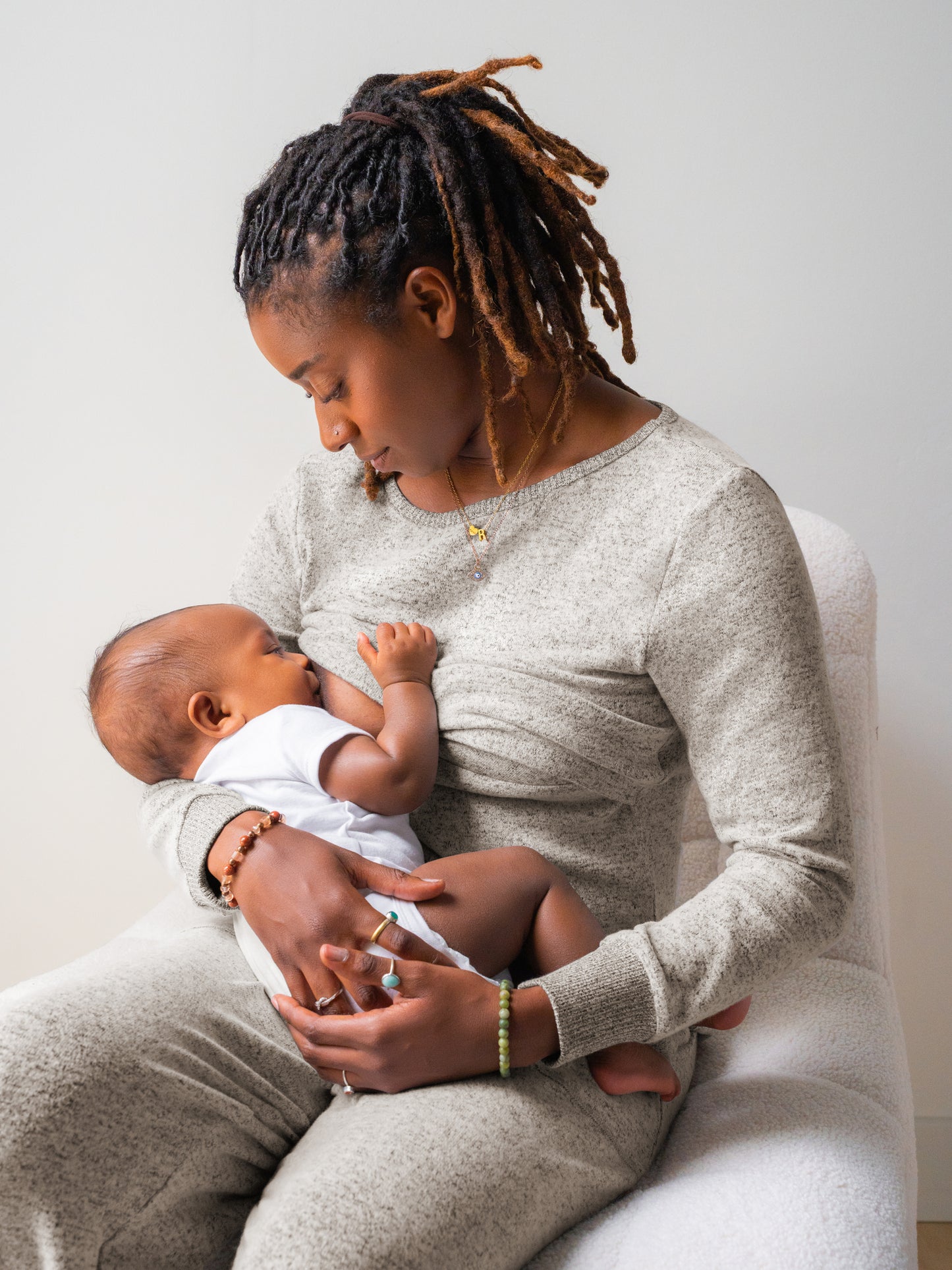 Model sitting on chair wearing the Zoe Nursing Pajama & Lounge Set in Grey Heather and nursing baby.