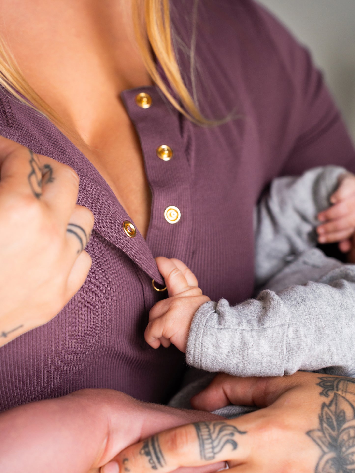 Close up of model wearing the Riley Ribbed Bamboo Maternity & Nursing Nightgown in Burgundy Plum, showing snaps in the front, with baby's fingers on neckline