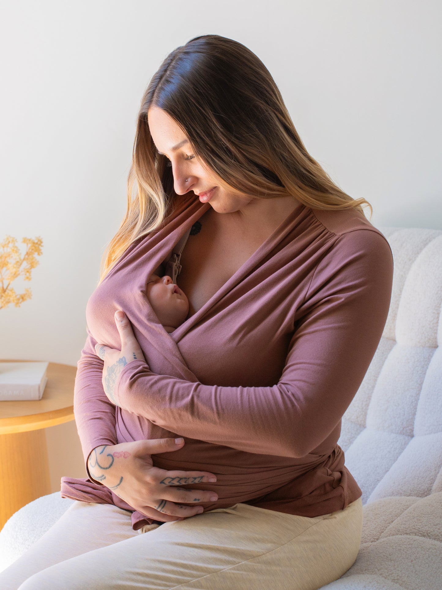 Model sitting in chair and wearing the Organic Cotton Skin to Skin Long Sleeve Wrap Top in Twilight, cradling baby who is wrapped in the top 
@model_info:Anna is wearing a Small.