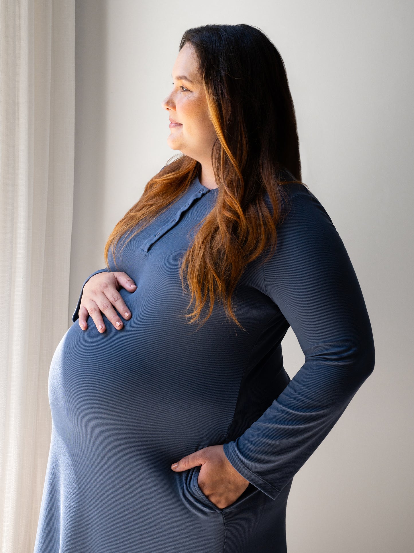 Side view of pregnant model wearing the Riley Ribbed Bamboo Maternity & Nursing Nightgown in Slate Blue, with hand in pocket.