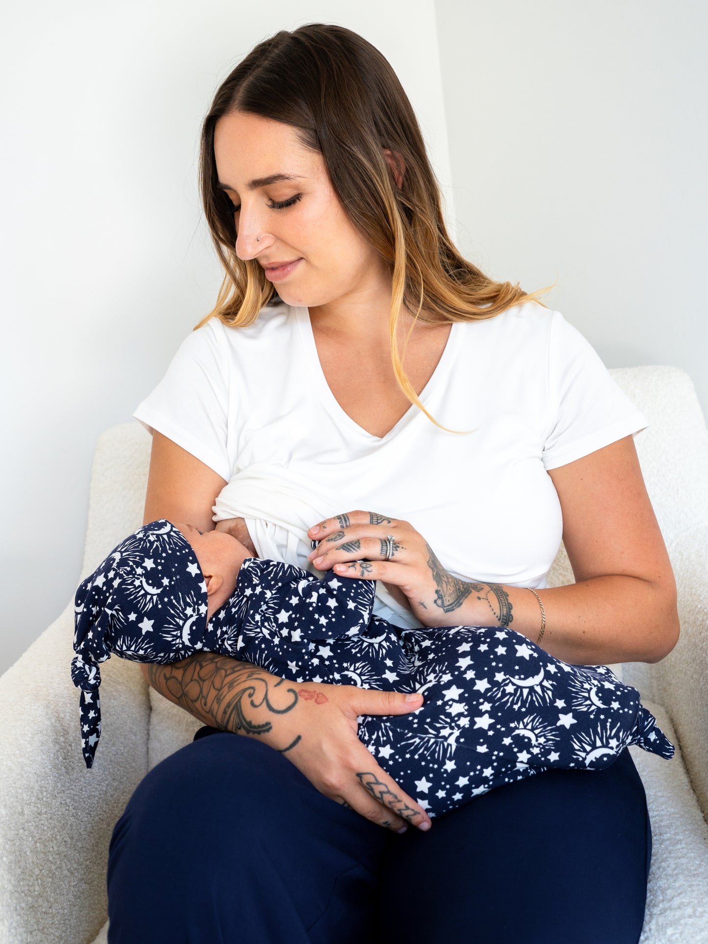 Model sitting and nursing baby who is wearing the Baby Knotted Gown & Hat Set in Navy Stars.