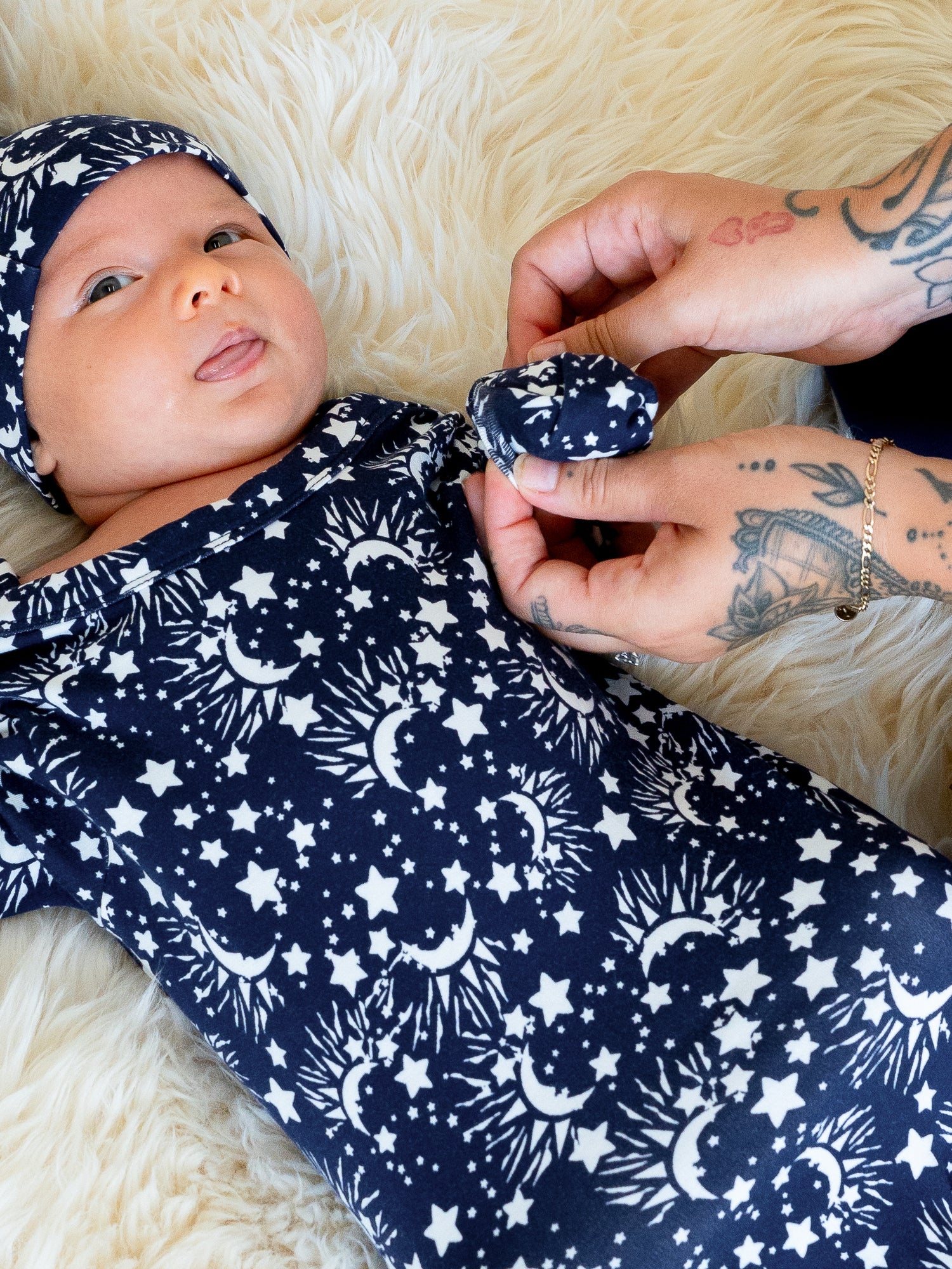 Newborn wearing the Baby Knotted Gown & Hat Set in Navy Stars, with mom putting cuff over one hand.