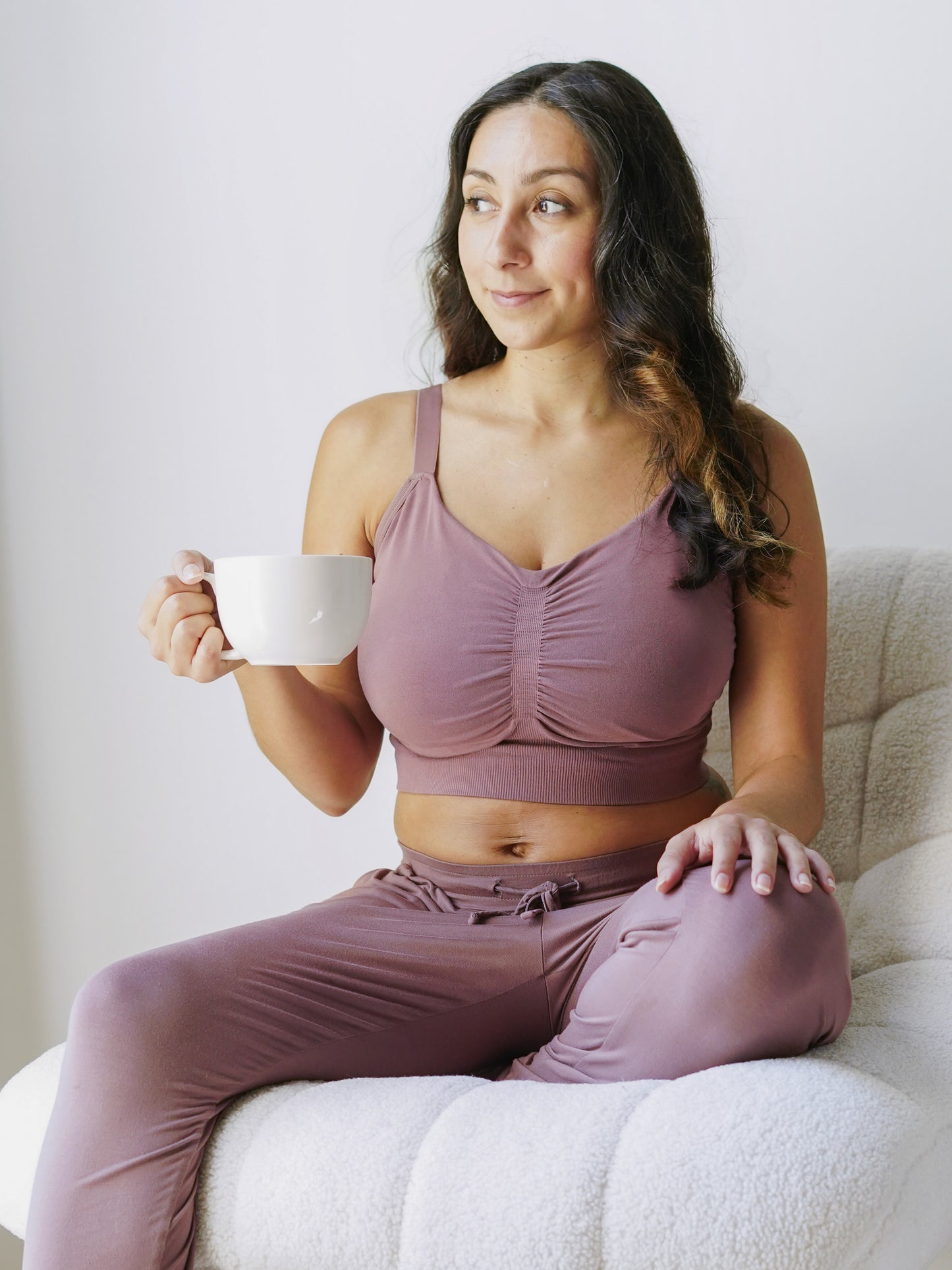 Model sitting in chair holding mug wearing the Sublime® Bamboo Hands-Free Pumping Lounge & Sleep Bra in Twilight @model_info:Daniella is wearing a Small Super Busty.