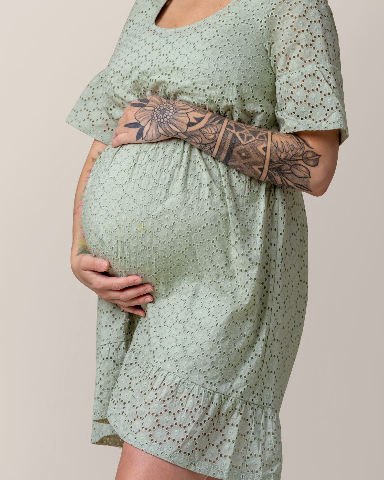 Cropped in view of pregnant model wearing the Dahlia Eyelet Maternity & Nursing Dress in Aqua Mist, cradling belly