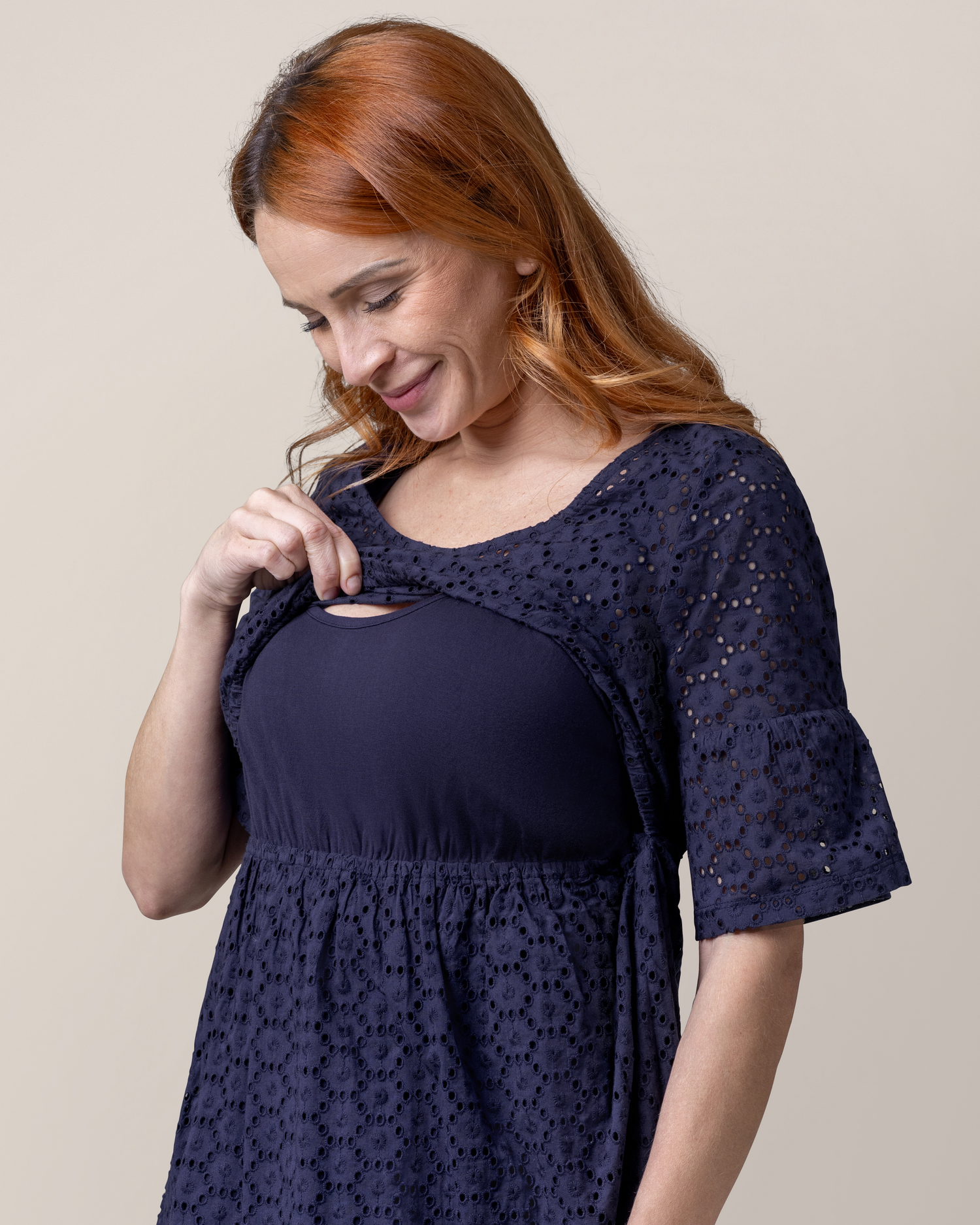 Cropped in view of model wearing the Dahlia Eyelet Maternity & Nursing Dress in Navy, pulling up top outer eyelet layer to show nursing access