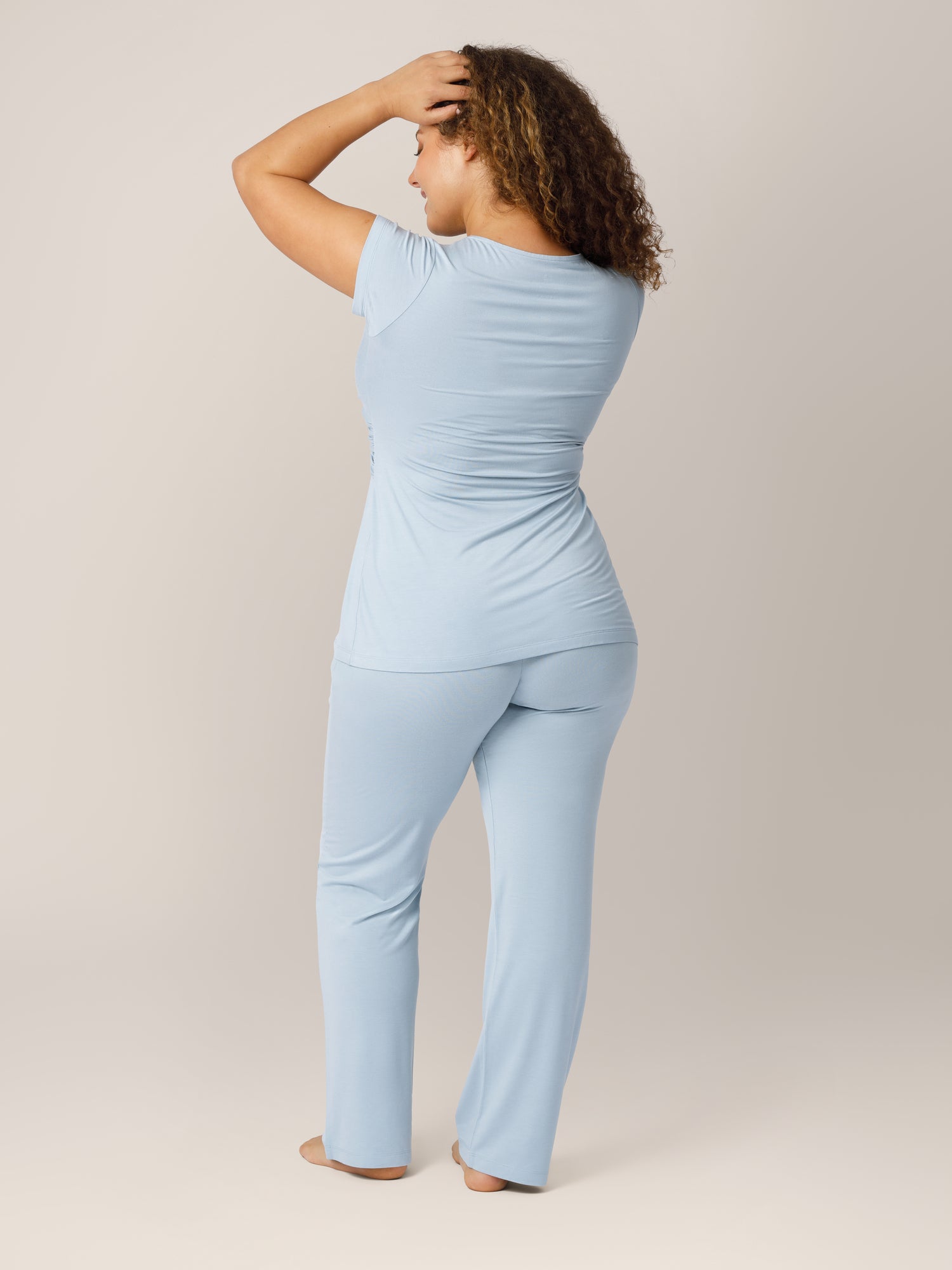 Back view of model wearing the Davy Maternity & Nursing Pajama Set in Mist, running hands through harir