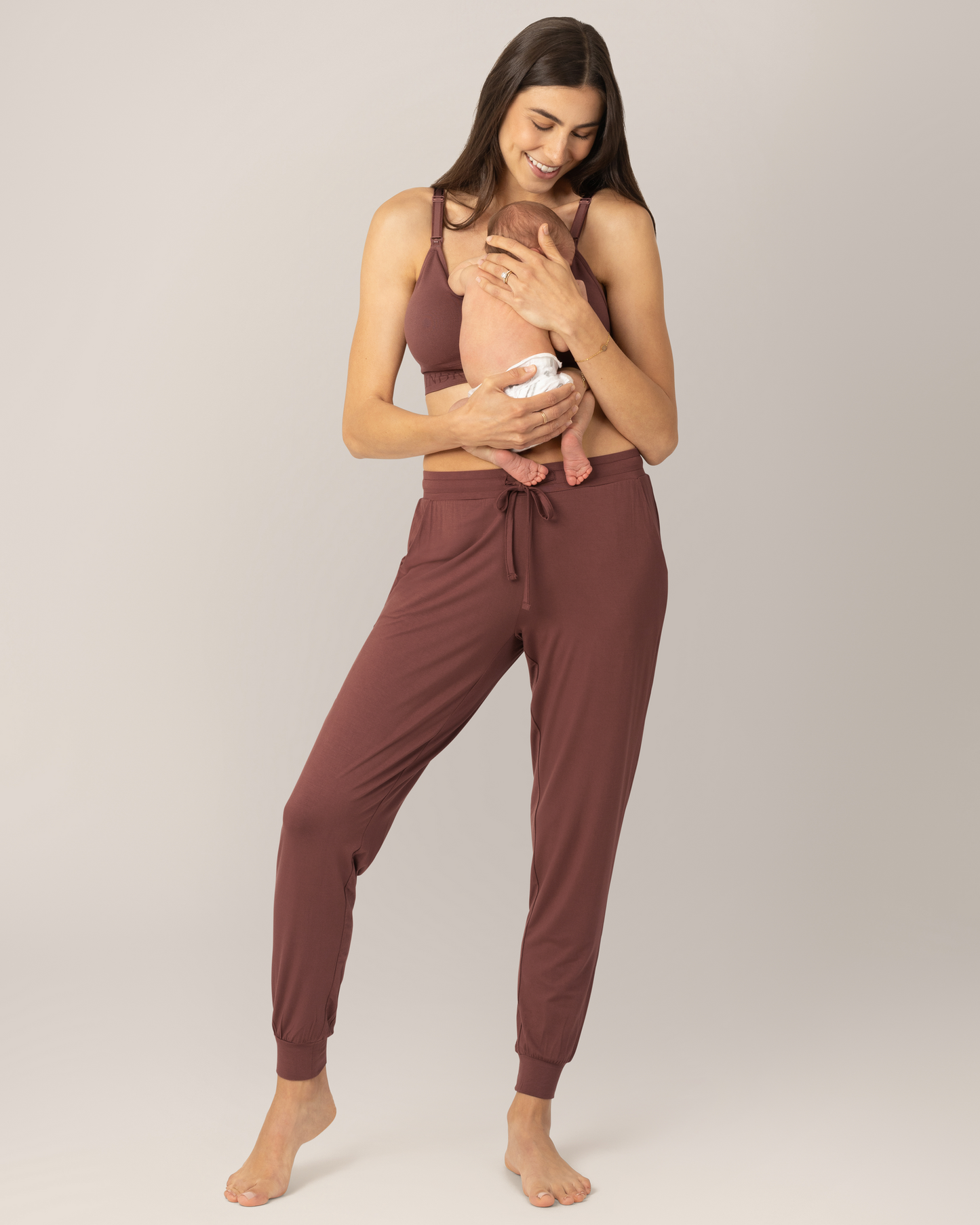 Front view of model wearing the Everyday Lounger Jogger in Redwood, holding baby against her.@model_info:Valerie is 5'10" and wearing a Small Long.