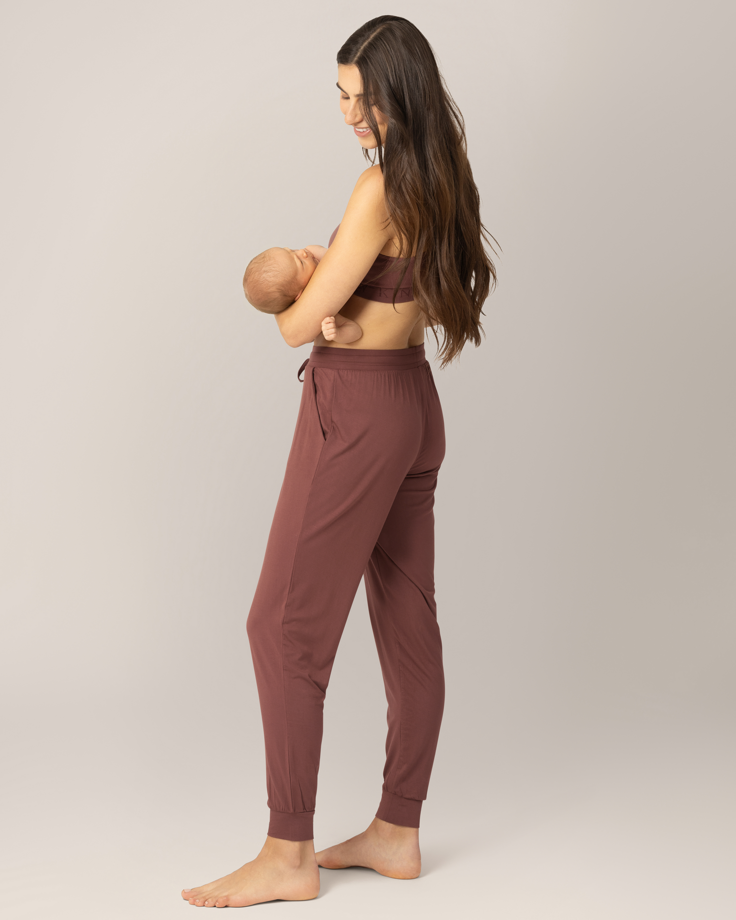 3/4 back view of model wearing the Everyday Lounger Jogger in Redwood, cradling baby.