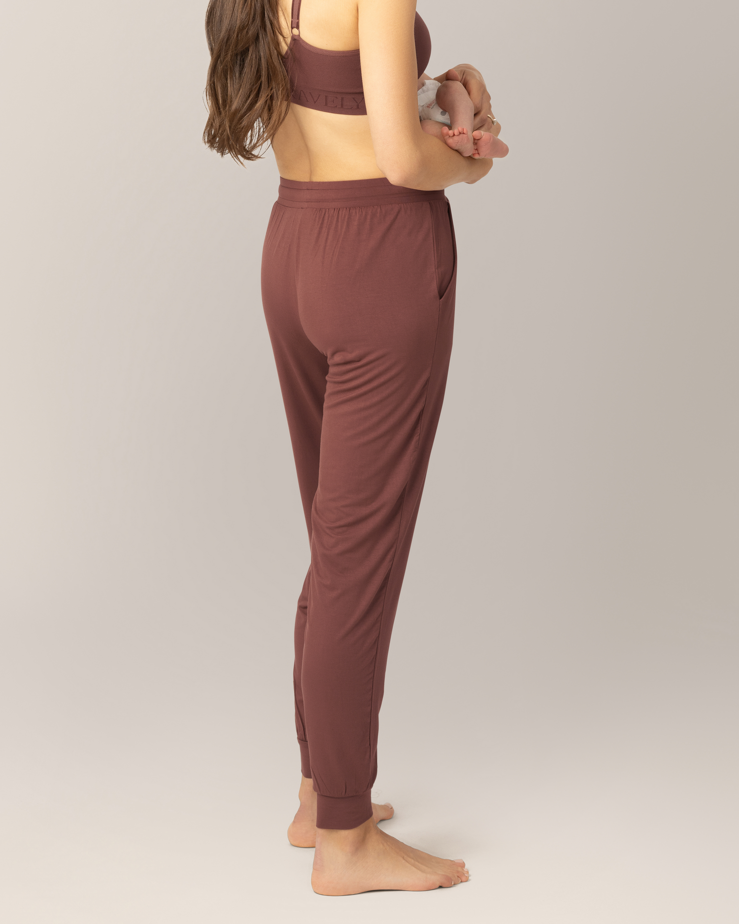 Close up back view of model wearing the Everyday Lounger Jogger in Redwood, cradling baby