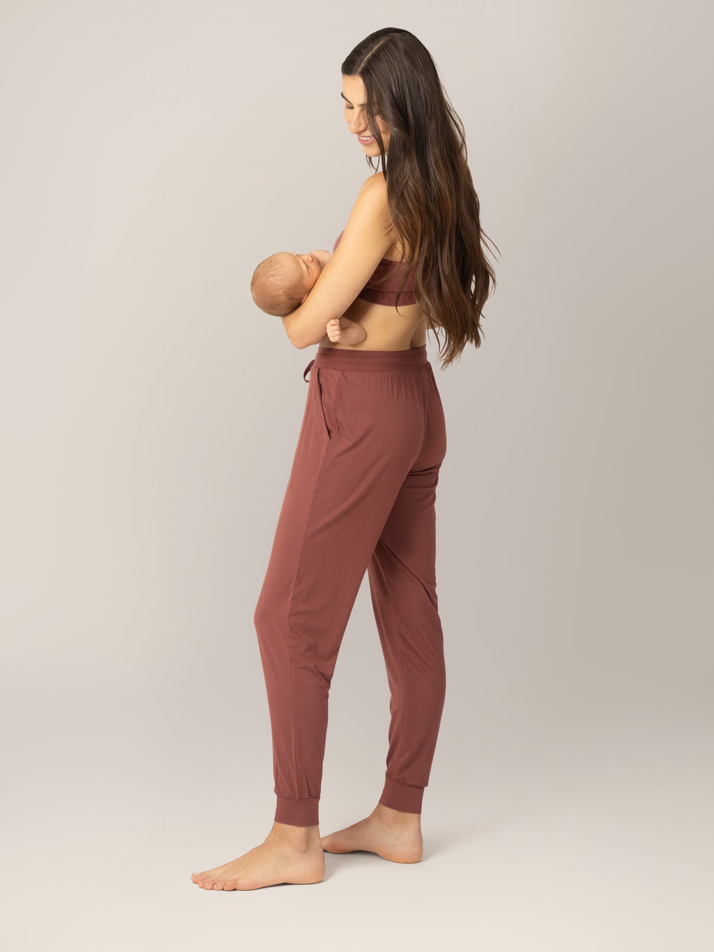 3/4 back view of model wearing the Everyday Lounger Jogger in Redwood, cradling babty.