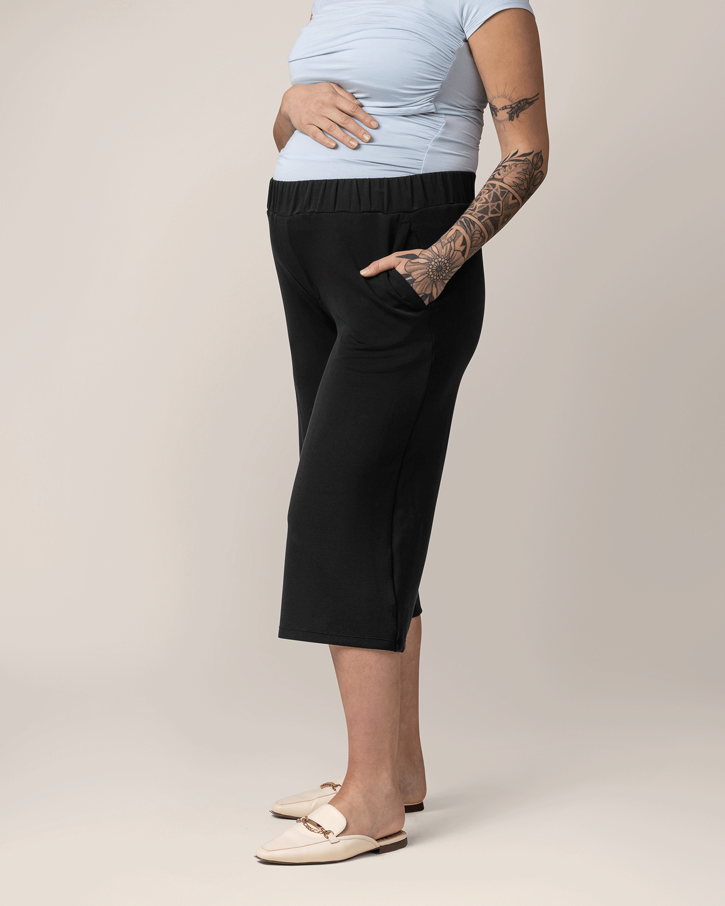 side view of pregnant model wearing Evie Maternity & Postpartum Pull-On Cropped Pant in black, with hand in pocket