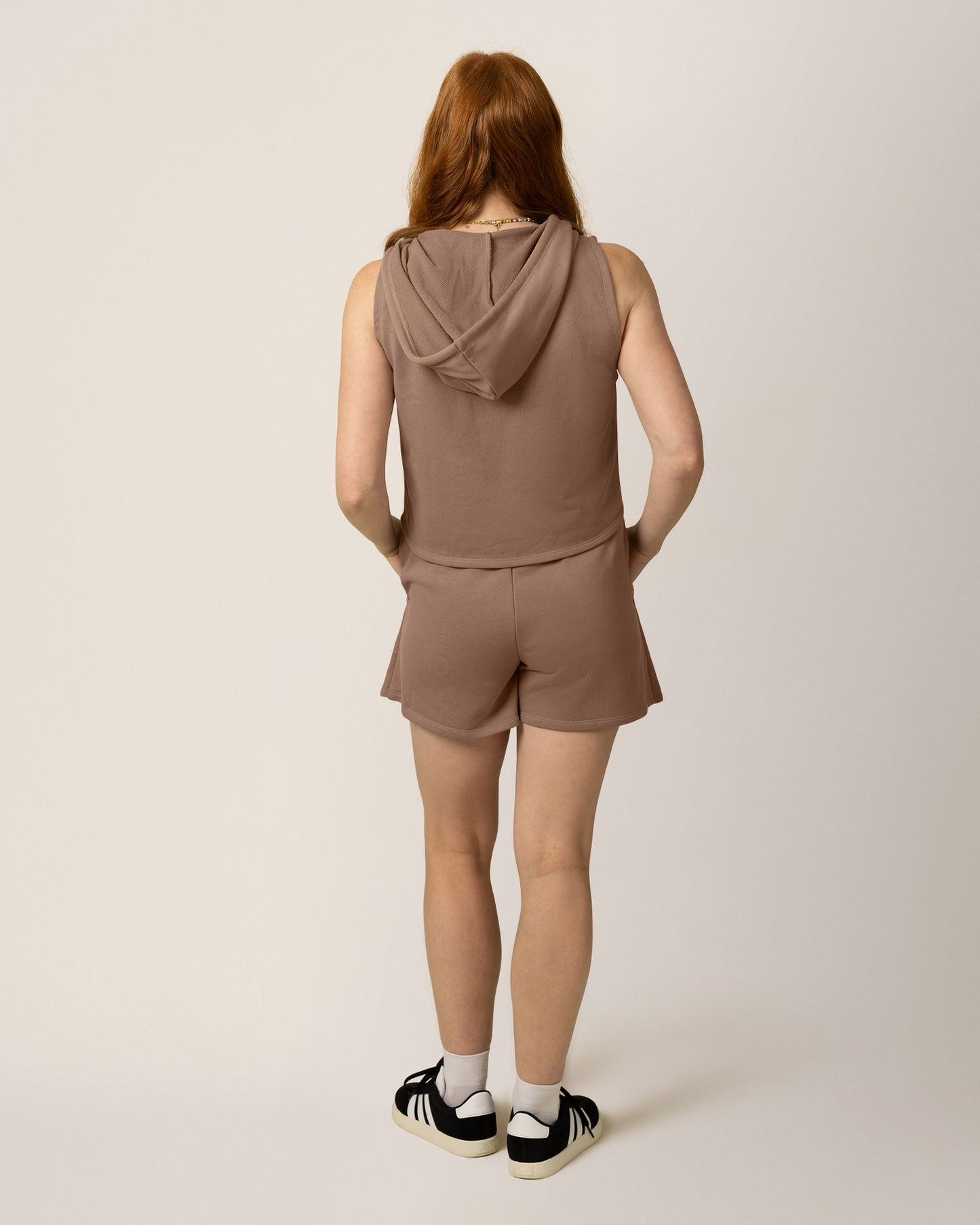 Back view of model wearing French Terry Sleeveless Nursing Hoodie in Taupe with matching French Terry On the Go Skort