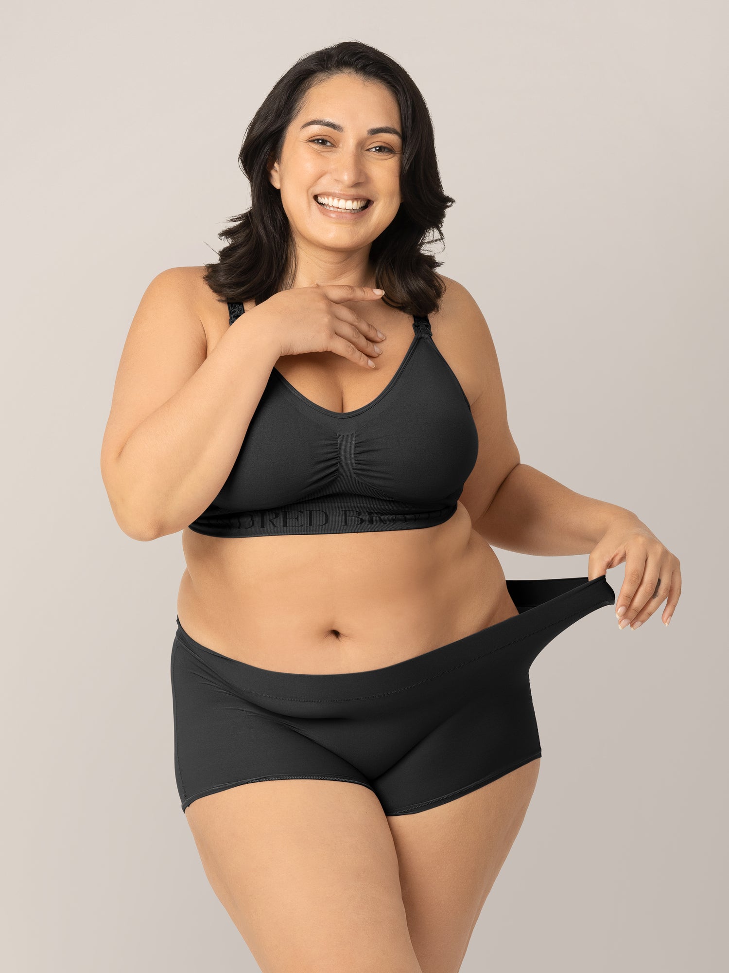 Model wearing the Black Grow with Me™ Maternity & Postpartum Boyshort and pulling the waistband to show stretch. @model_info: Connie is wearing an X-Large. 