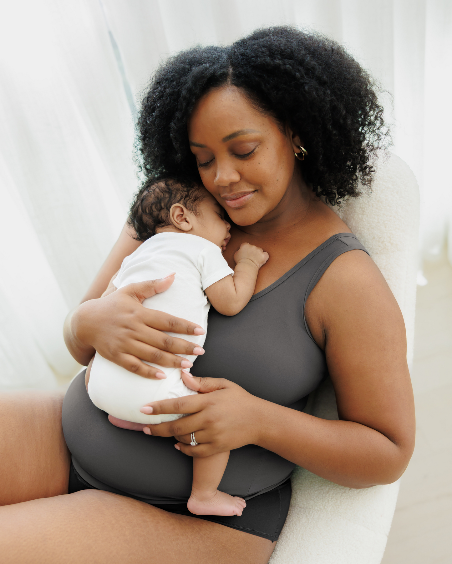 Model sitting on chair cradling baby against chest and wearing the Grow with Me™ Maternity & Nursing Tank in Stormy Grey