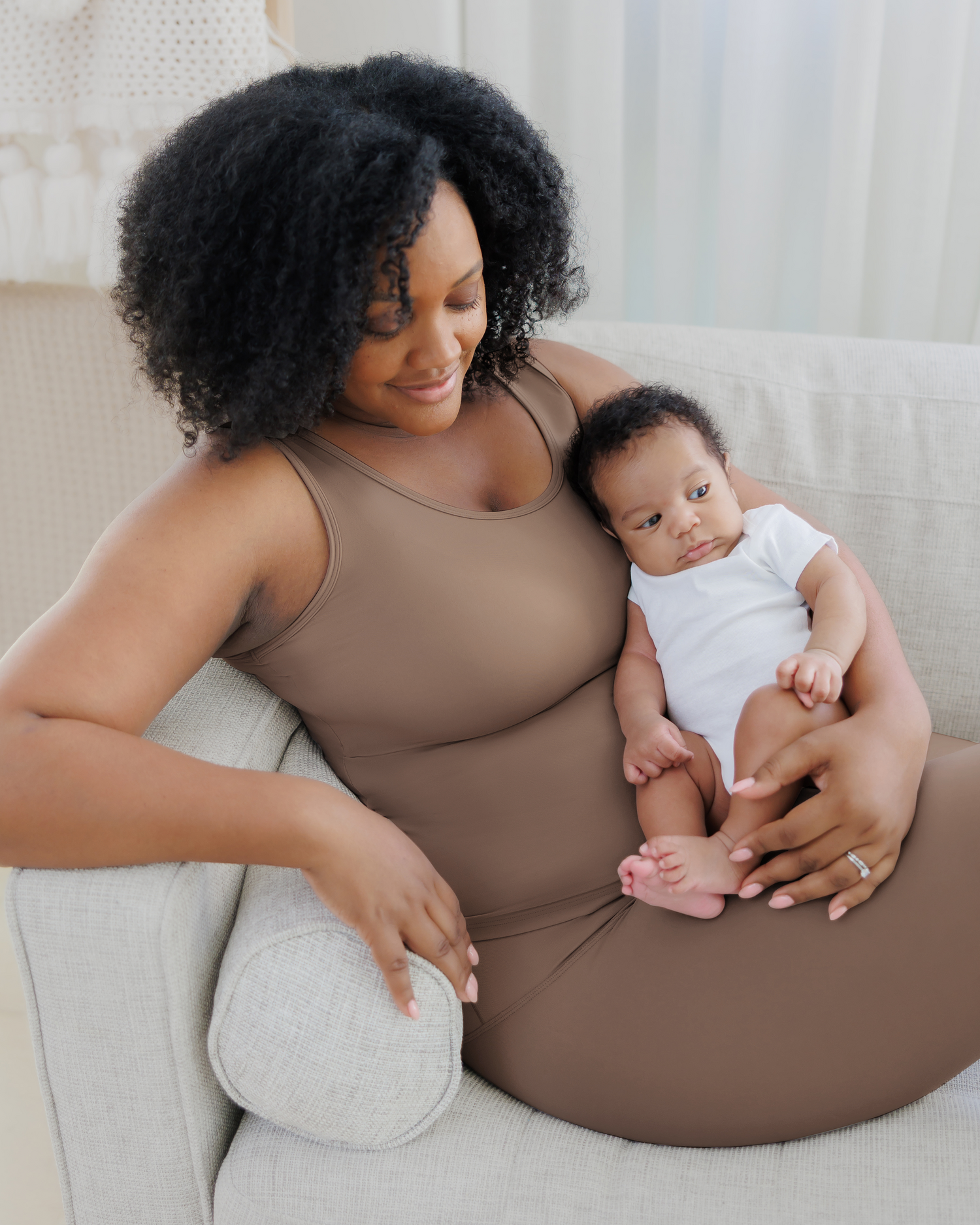 Model on sofa cradling baby, wearing the Grow with Me™ Maternity & Nursing Tank in Taupe paired with matching Grow with Me™ Maternity & Postpartum Legging 