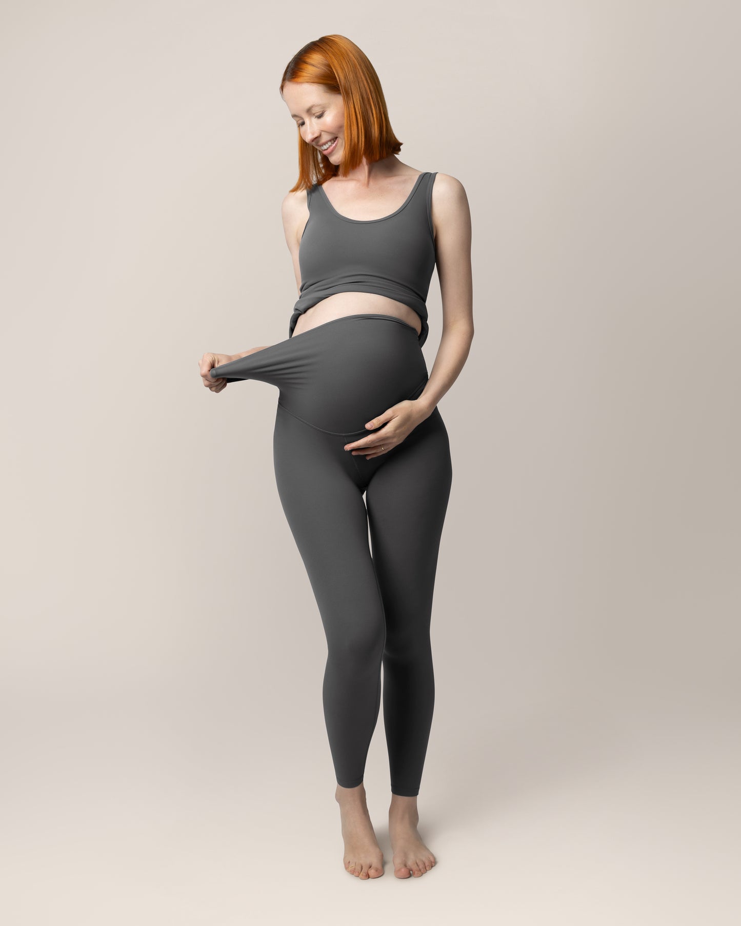 Front view of pregnant model wearing the Grow with Me™ Maternity & Postpartum Legging in Stormy Grey, showing stretch of waistband and paired with matching Grow with Me™ Maternity & Nursing Tank @model_info:Anna is 5'10" and wearing a Small.