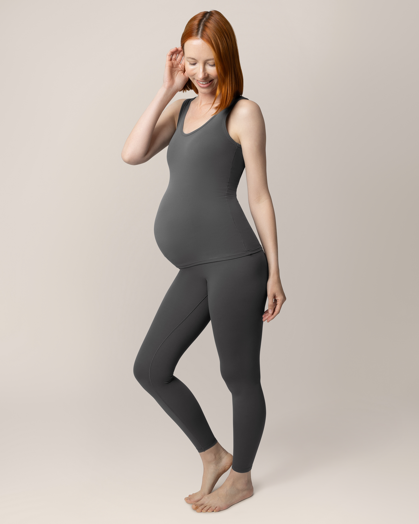 3/4 view of pregnant model wearing the Grow with Me™ Maternity & Postpartum Legging in Stormy Grey paired with matching Grow with Me™ Maternity & Nursing Tank