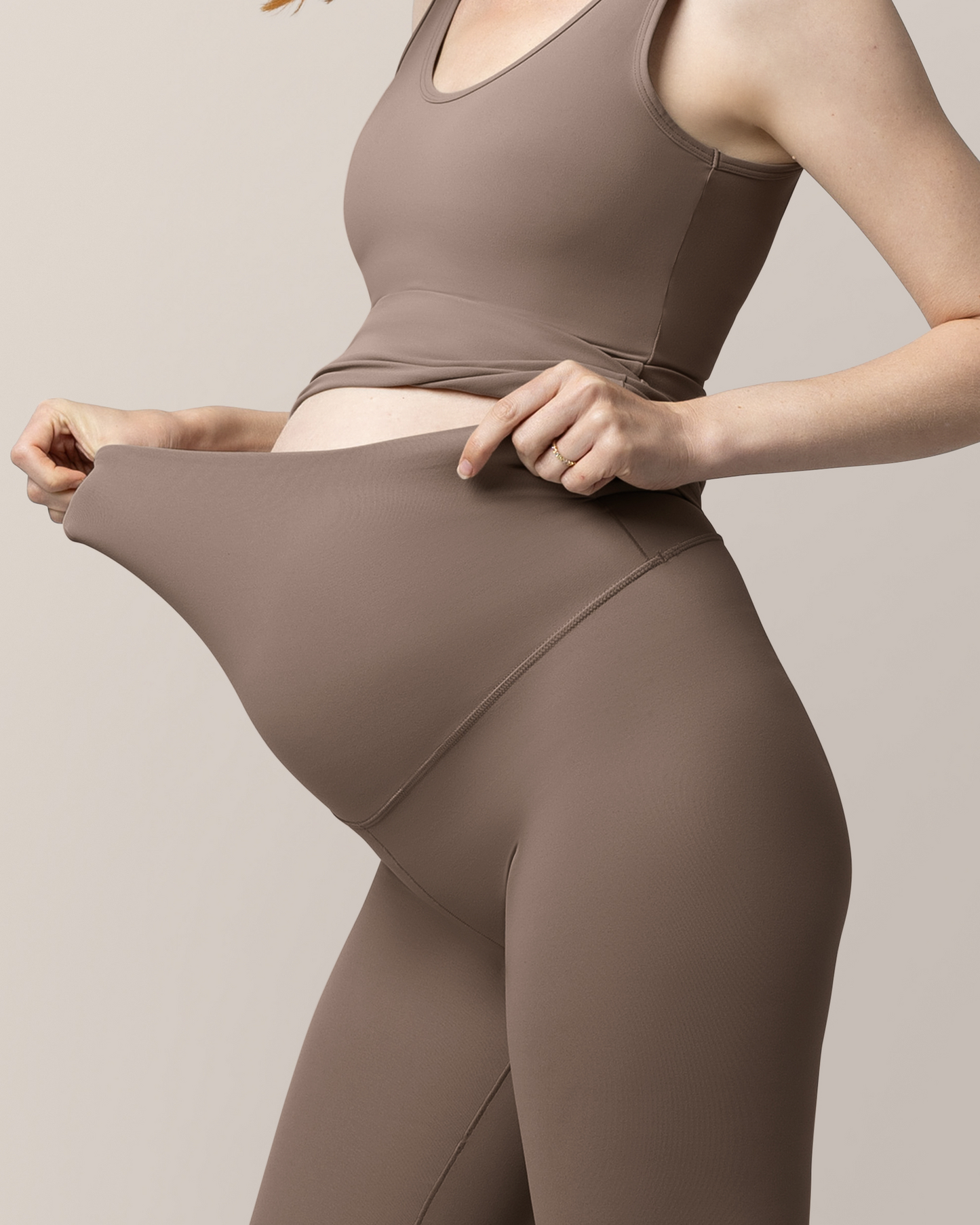 Close up view of pregnant model wearing the Grow with Me™ Maternity & Postpartum Legging in Taupe, showing stretch of the waistband