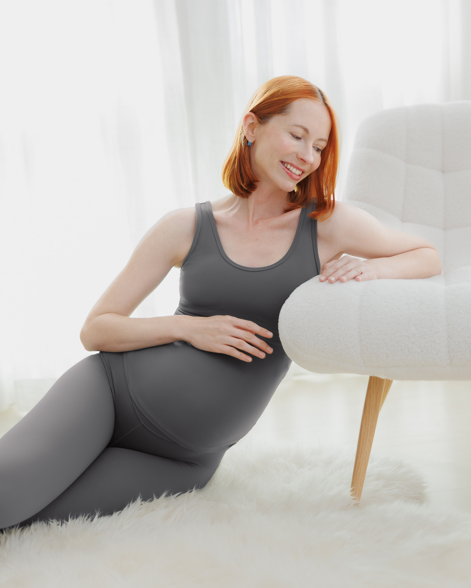 Pregnant model leaning on chair wearing the Grow with Me™ Maternity & Nursing Tank in Stormy Grey, paired with matching Grow with Me™ Maternity & Postpartum Legging @model_info:Anna is wearing a Small.