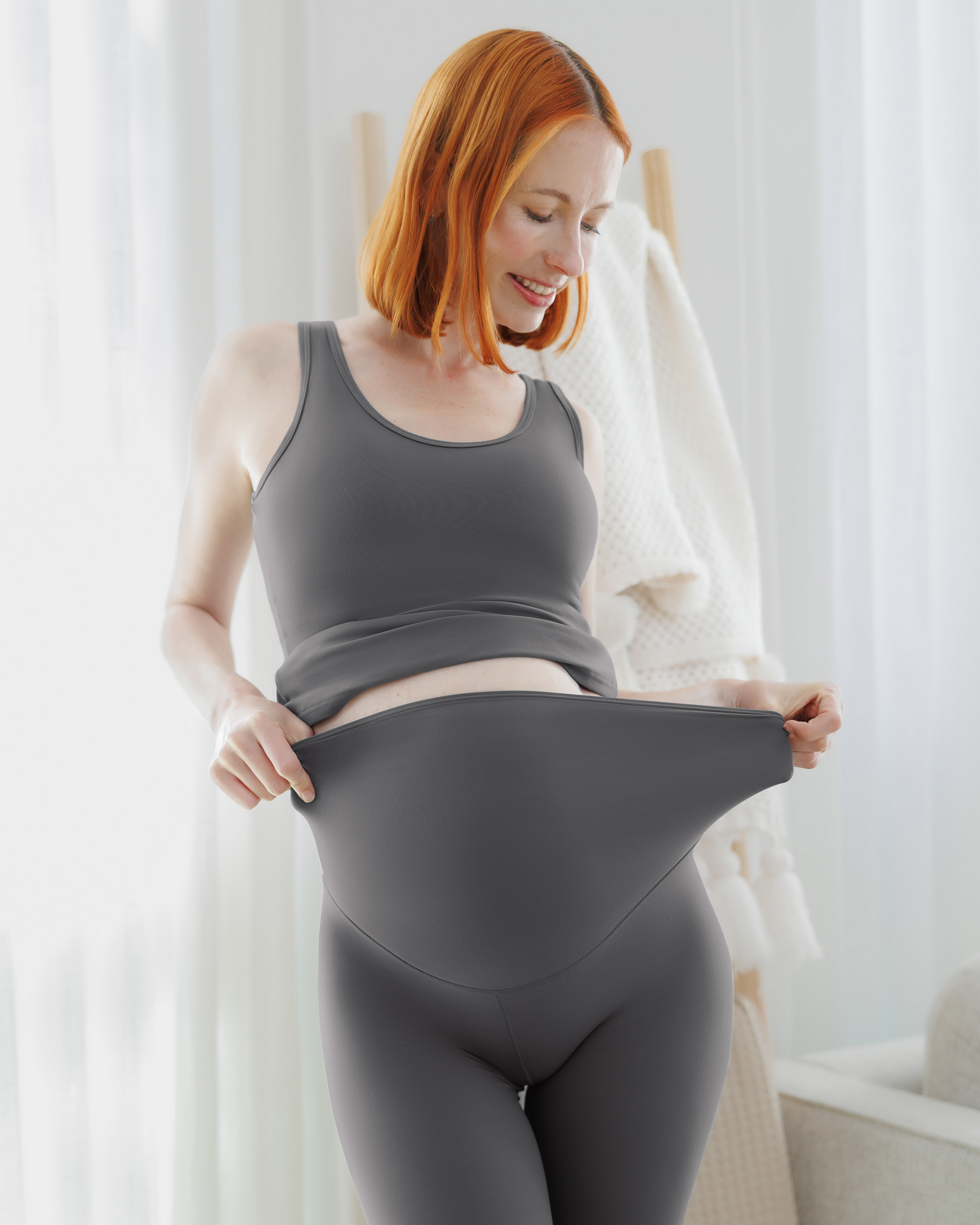 Close up front view of pregnant model wearing the Grow with Me™ Maternity & Postpartum Legging in Stormy Grey showing stretch of waistband, paired with matching Grow with Me™ Maternity & Nursing Tank