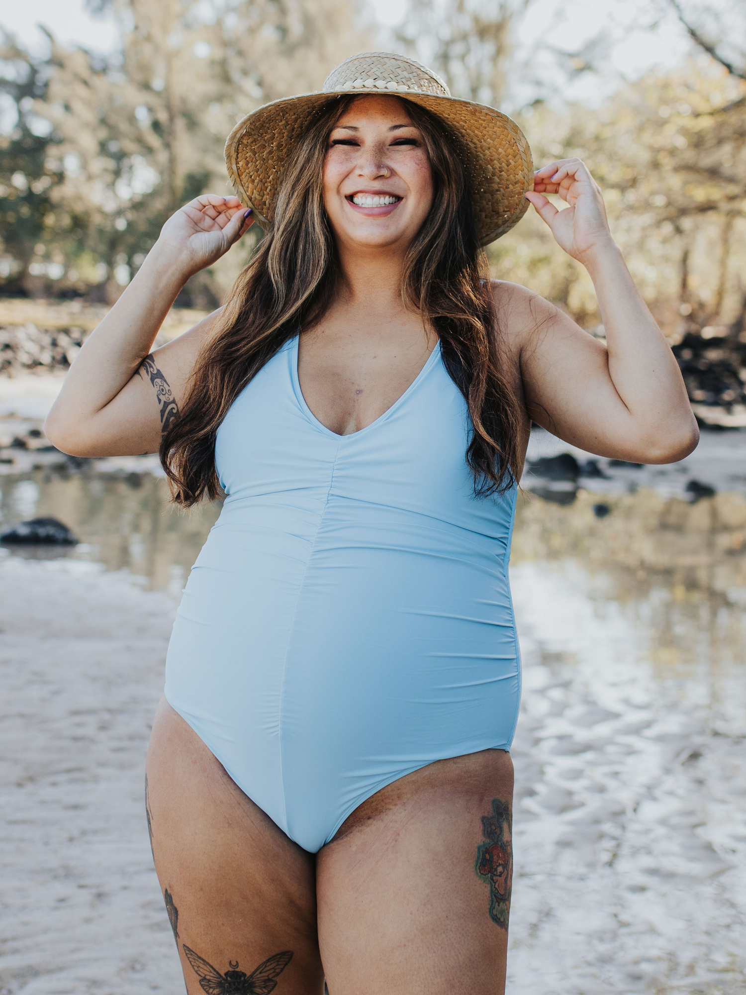 Front view of model wearing the Gathered Maternity One Piece Swimsuit in Light Blue, holding onto to brim of sun har. @model_info: Kyllie is wearing an X-Large.