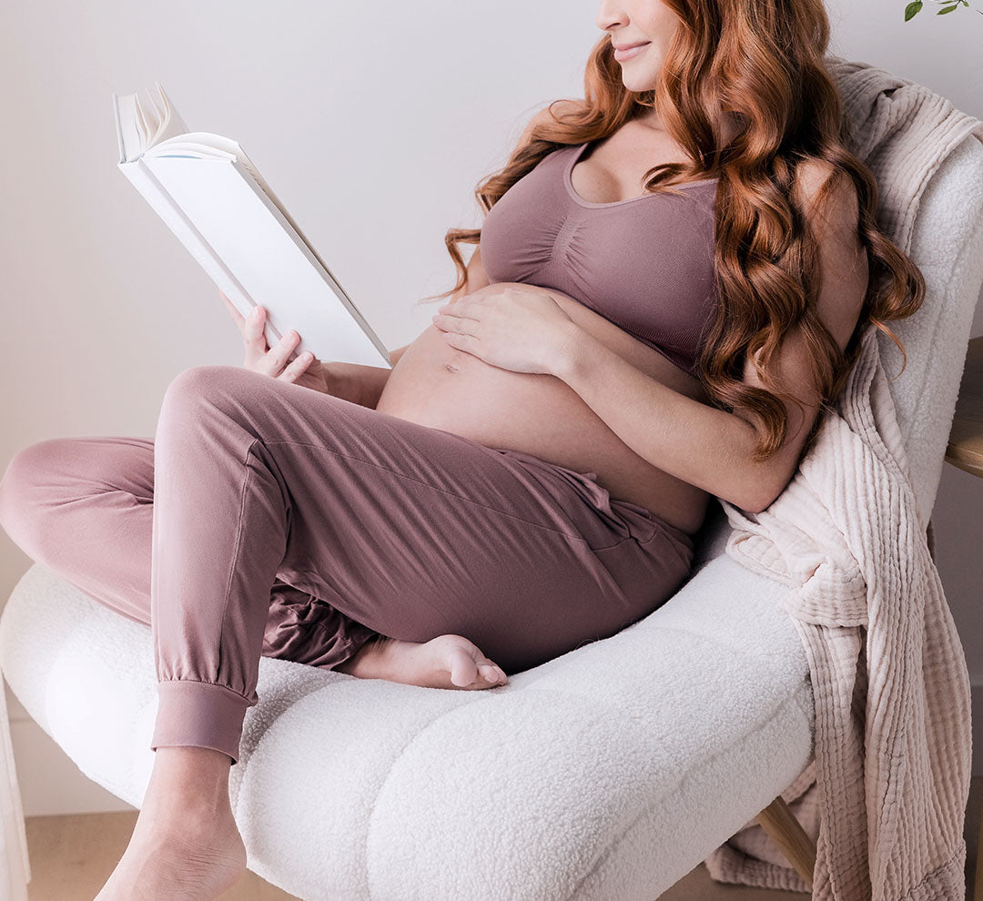 Pregnant model sitting in chair reading book, wearing the Everyday Lounge Jogger in Twilight, paired with matching Simply Sublime Nursing Bra