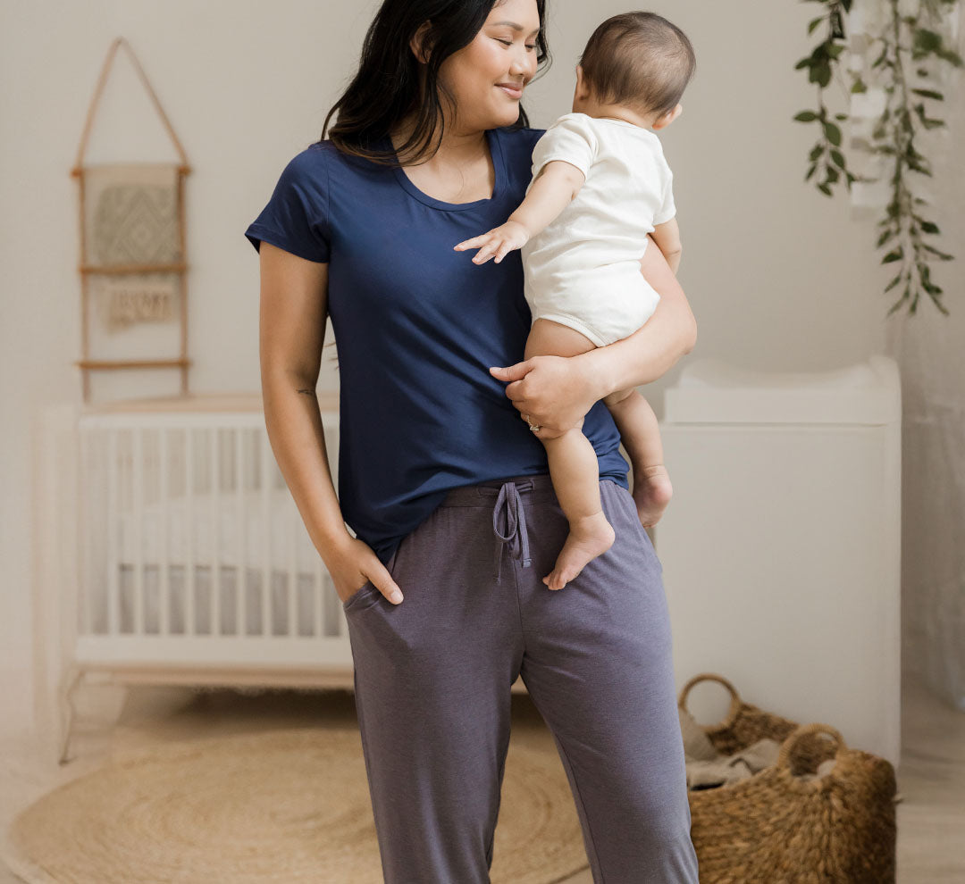 Model wearing the Everyday Lounge Jogger in Granite, paired with the Everyday Maternity & Nursing T-shirt in Navy, holding baby