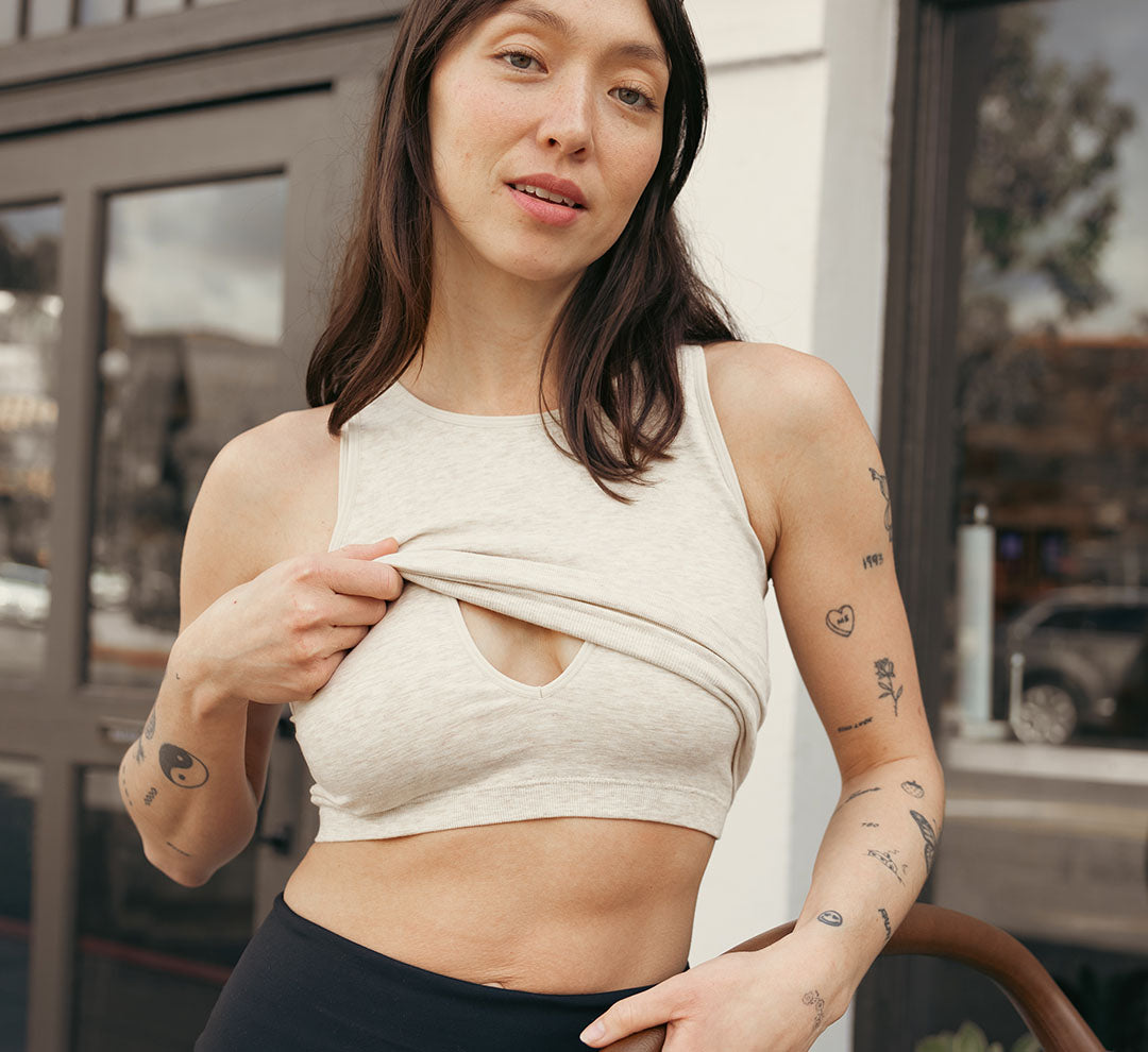 Model wearing the Sublime® Bamboo Maternity & Nursing Longline Bra in Oatmeal Heather, lifting outer layer to show nursing access