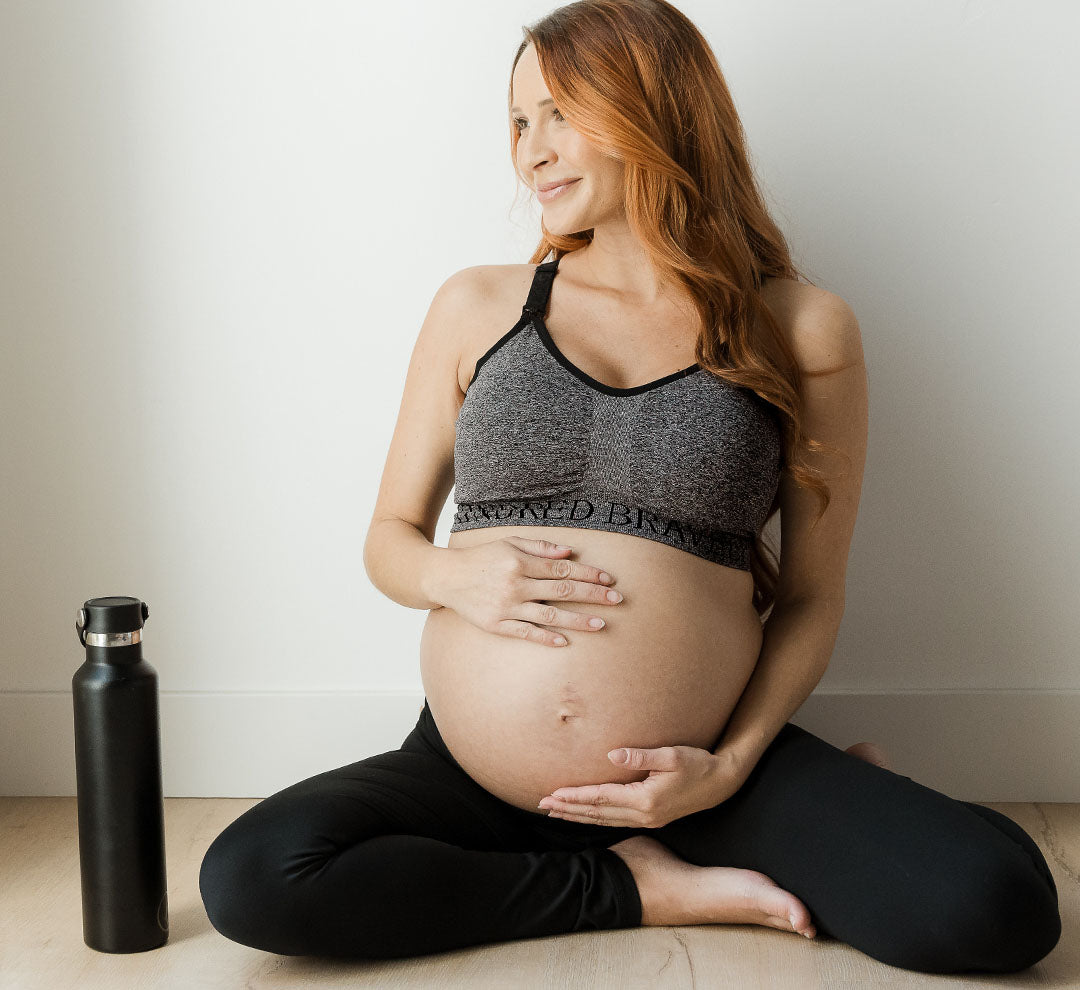 Pregnant model sitting on floor wearing the Sublime® Nursing Sports Bra in Grey Heather