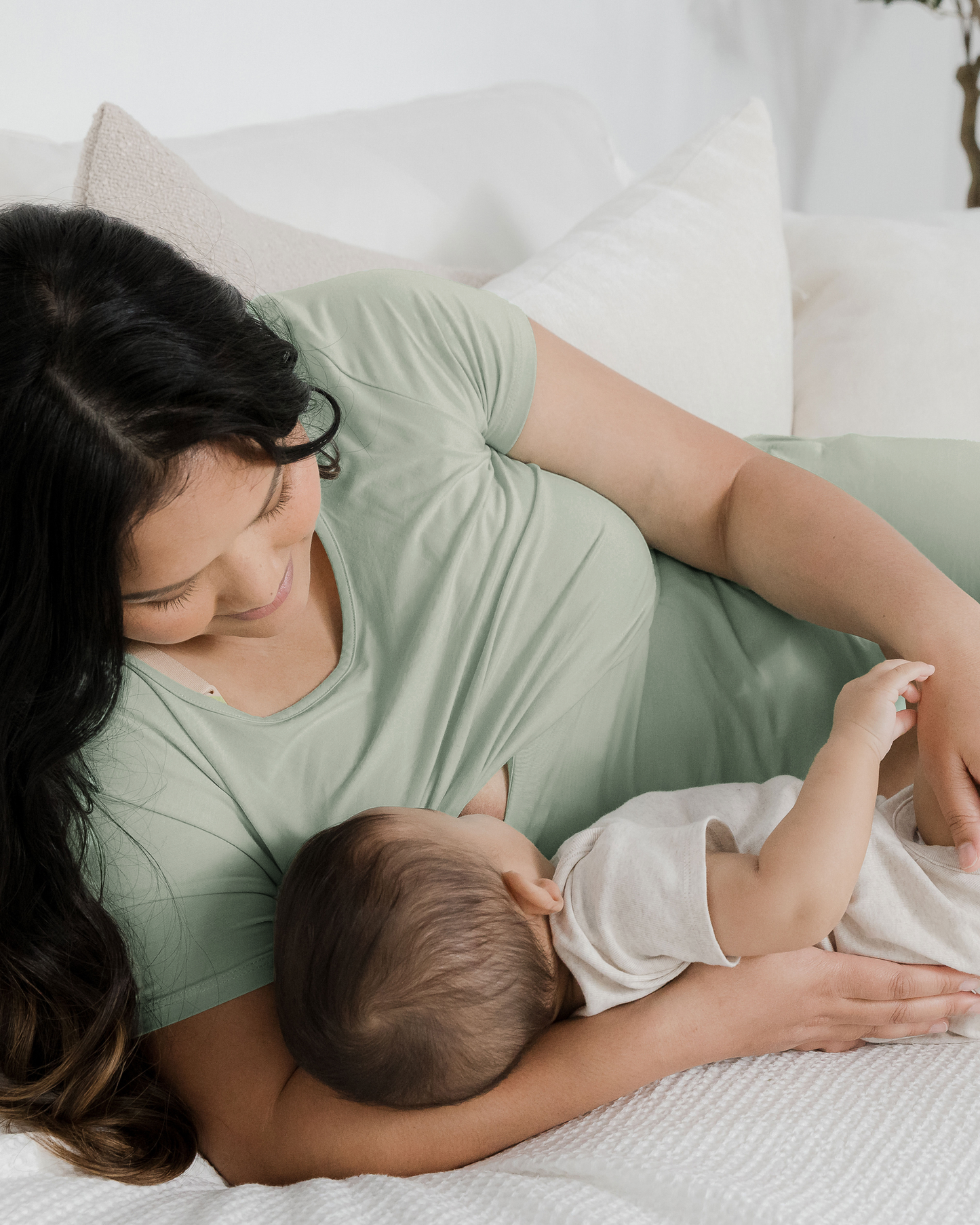 Model laying on bed nursing baby while wearing the Eleanora Bamboo Maternity & Nursing Dress in Aqua Mist @model_info:Binc is 5'5" and wearing a Medium.