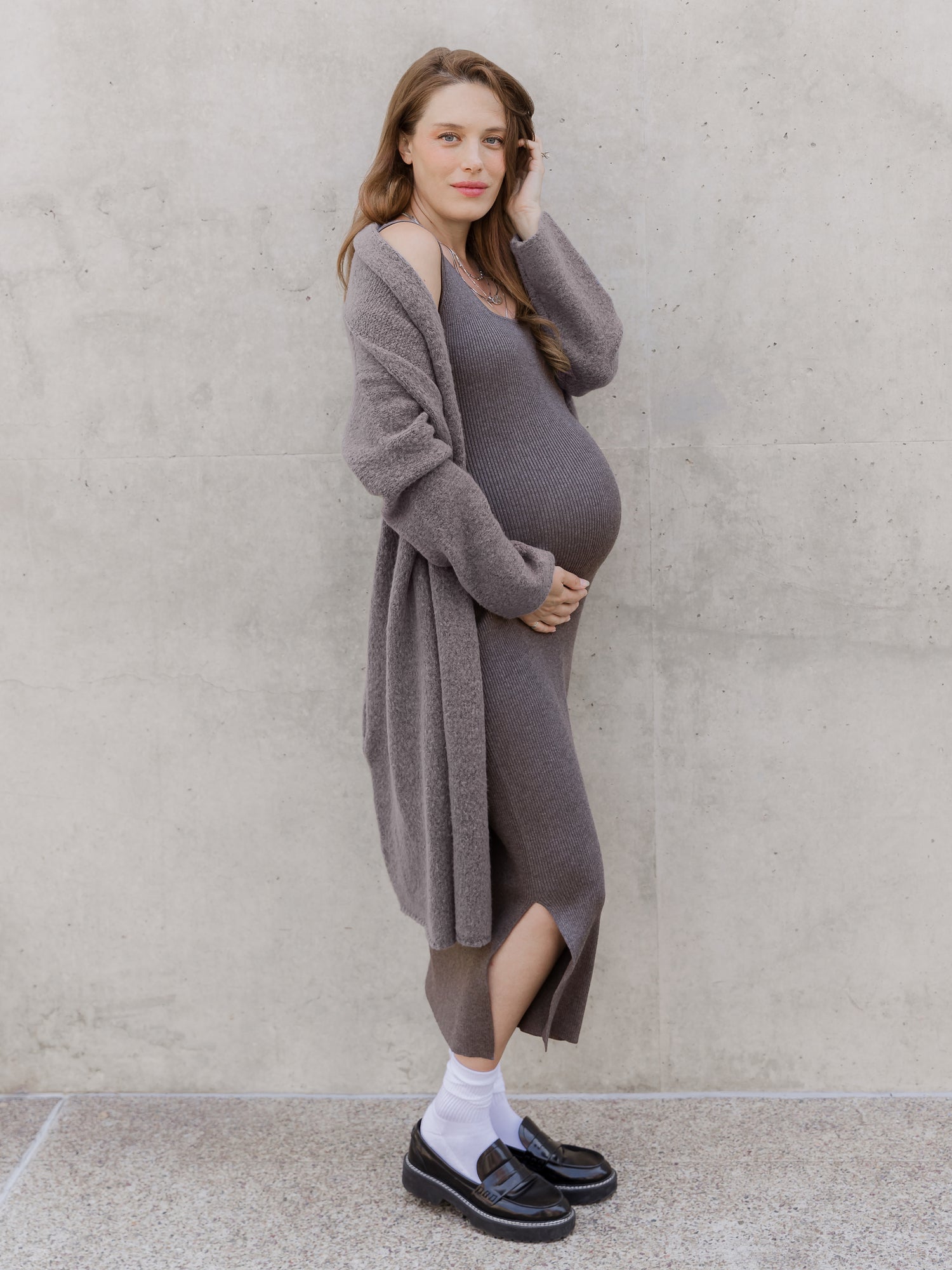 Side view of pregnant model outside wearing the 2-in-1 Maternity & Nursing Midi Dress in Charcoal, paired with the Chloe Cardigan Sweater