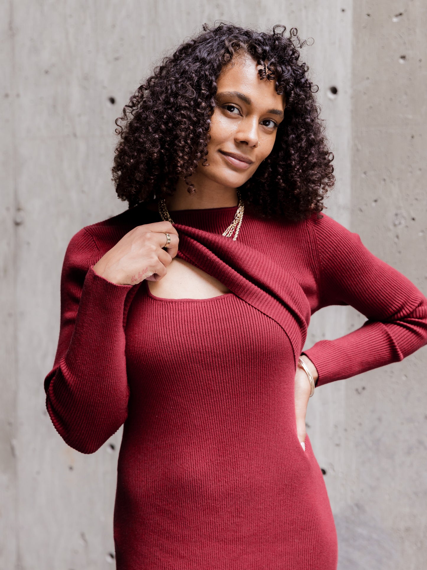 Front view of model wearing the 2-in-1 Maternity & Nursing Midi Dress in Garnet, lifting outer long-sleeve cropped layer